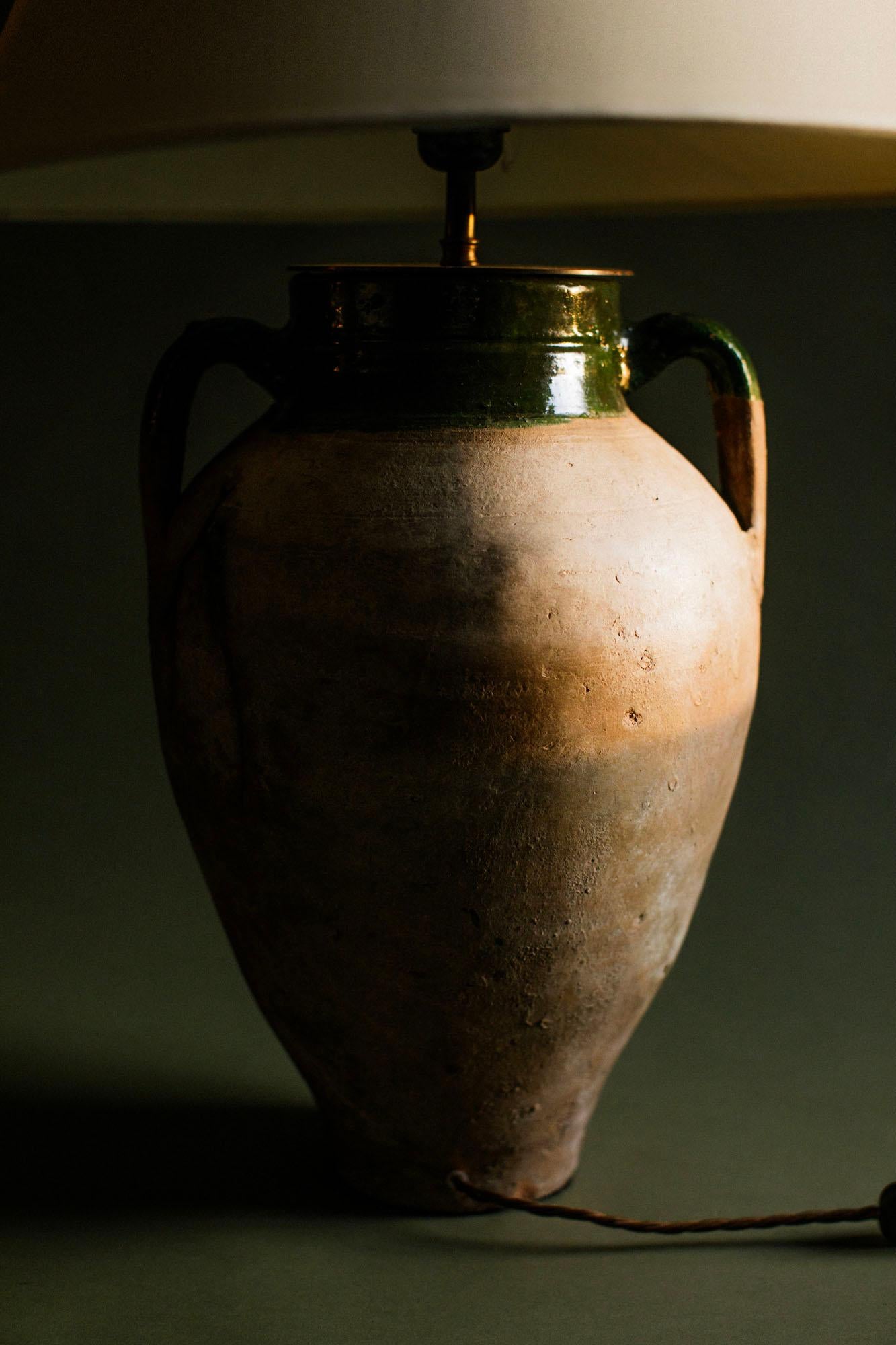 Lámpara de mesa turca vintage de terracota, fabricada a mano en el siglo XX con técnicas tradicionales de Anatolia. Esta lámpara presenta un característico borde vidriado en verde y un cuerpo de terracota natural, con marcas superficiales y pátina