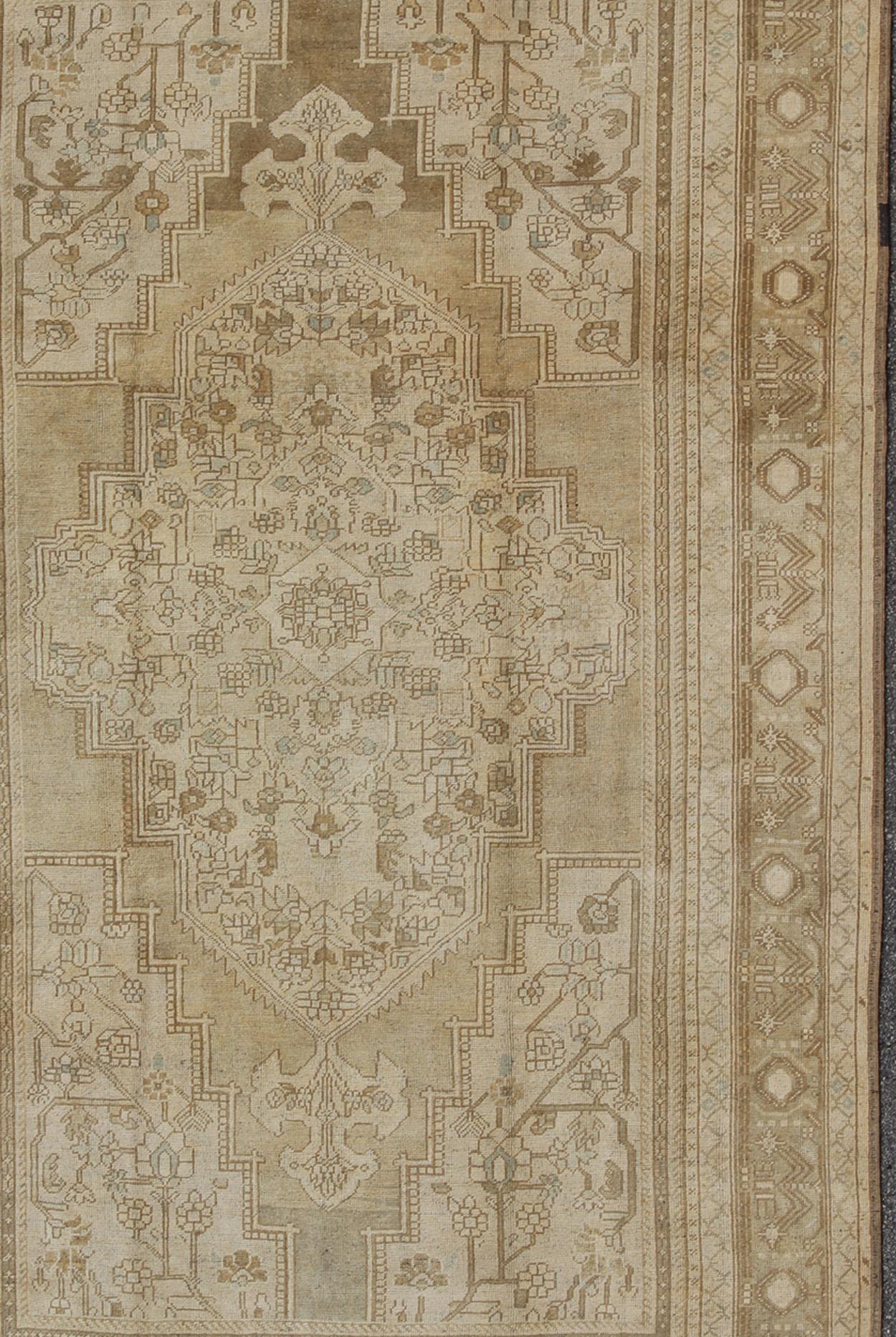Measures: 7'3 x 13'

This muted Turkish Oushak features a light khaki border and background with shades of beige. The corners and central medallion are composed of a light camel and very subtle blue accents within floral motifs decorating the field