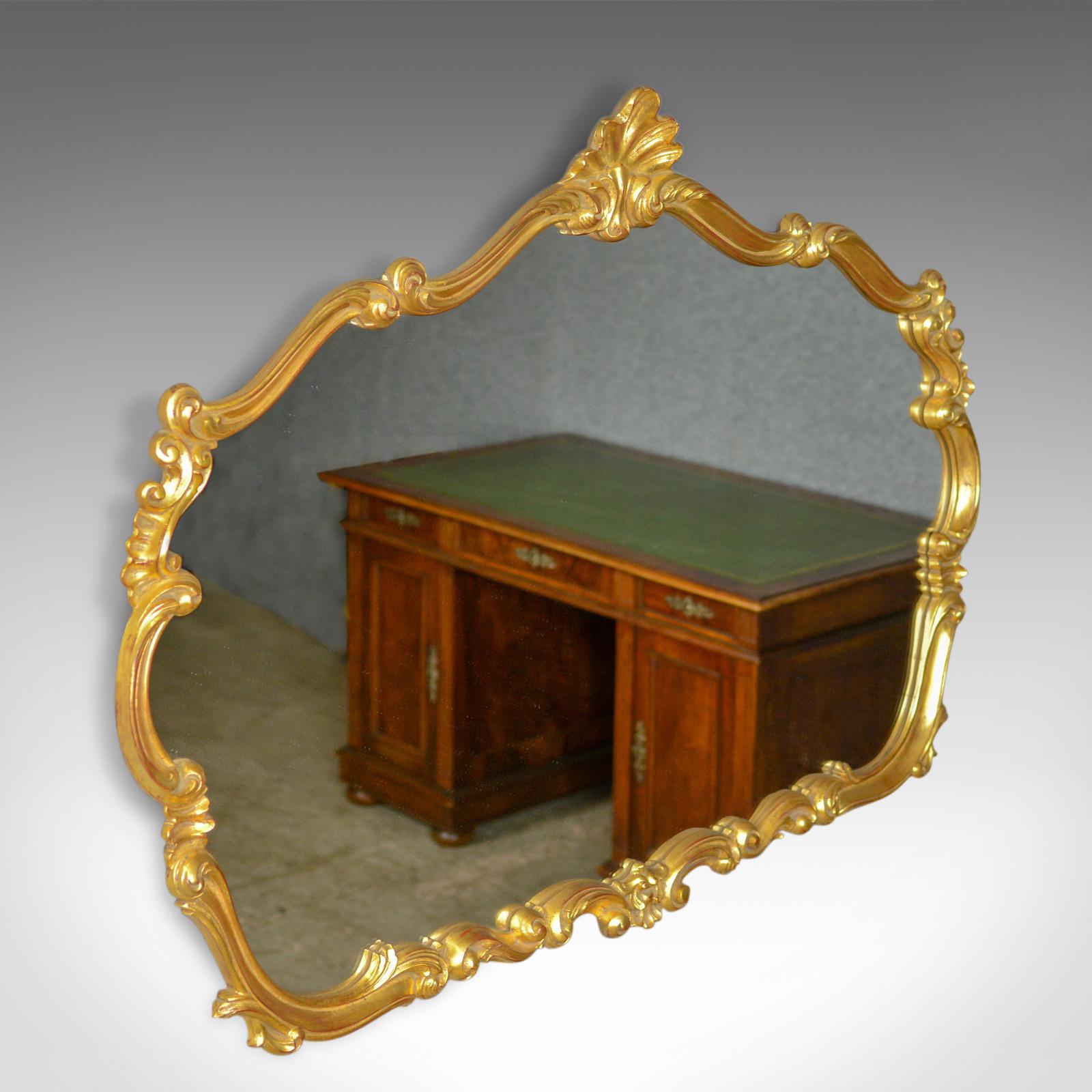 This is a large, vintage wall mirror in the Victorian Rococo Revival manner, English dating to the latter part of the 20th century.

Typically elaborate and elegant design
Gilt frame featuring scrolls, leaves and embellishment
Quality shaped