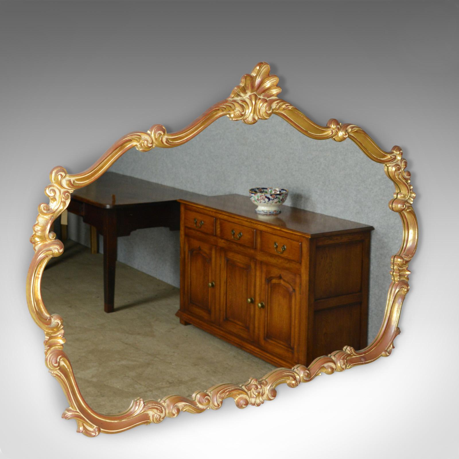 This is a large, vintage wall mirror in the Victorian Rococo revival taste, English dating to the latter part of the 20th century.

Typically elaborate and elegant design
Gilt frame featuring scrolls, leaves and embellishment
Quality shaped