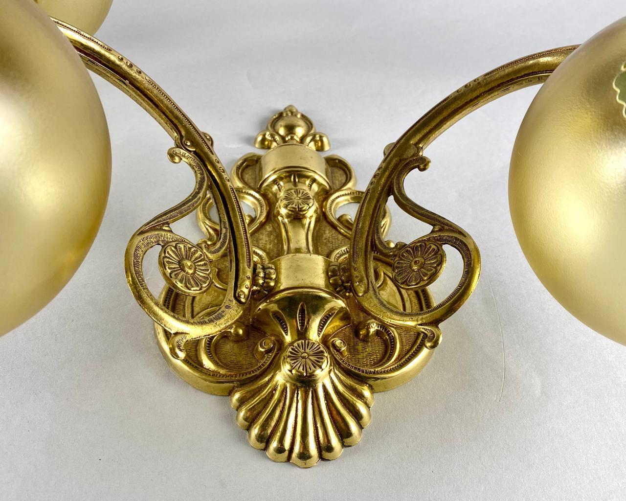 Incredible Art Nouveau style double arm wall sconces are perfect for wall mounting in a living room of classic style.

Body of large wall lamps in brass with cast horns, round glass shades in gold color with a beautiful green floral