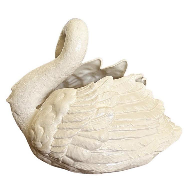 A very large vintage ceramic swan planter. This piece is created from ceramic and glazed in a creamy white glaze. The vessel depicts a swan with its long neck nestled into its feathers. The opening is at the top and between his wings. He had painted