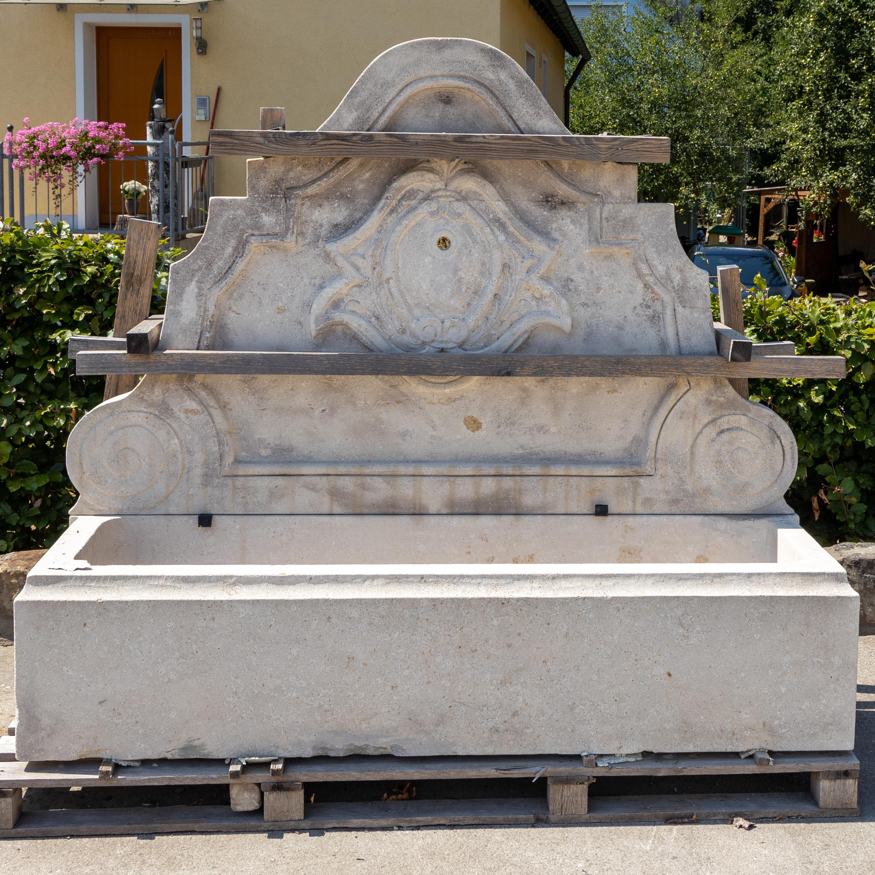 Large wall fountain made of Pietra di Vicenza with rectangular basin and curved back wall with volute decoration and central cartouche. Basin Height: 45 cm.
