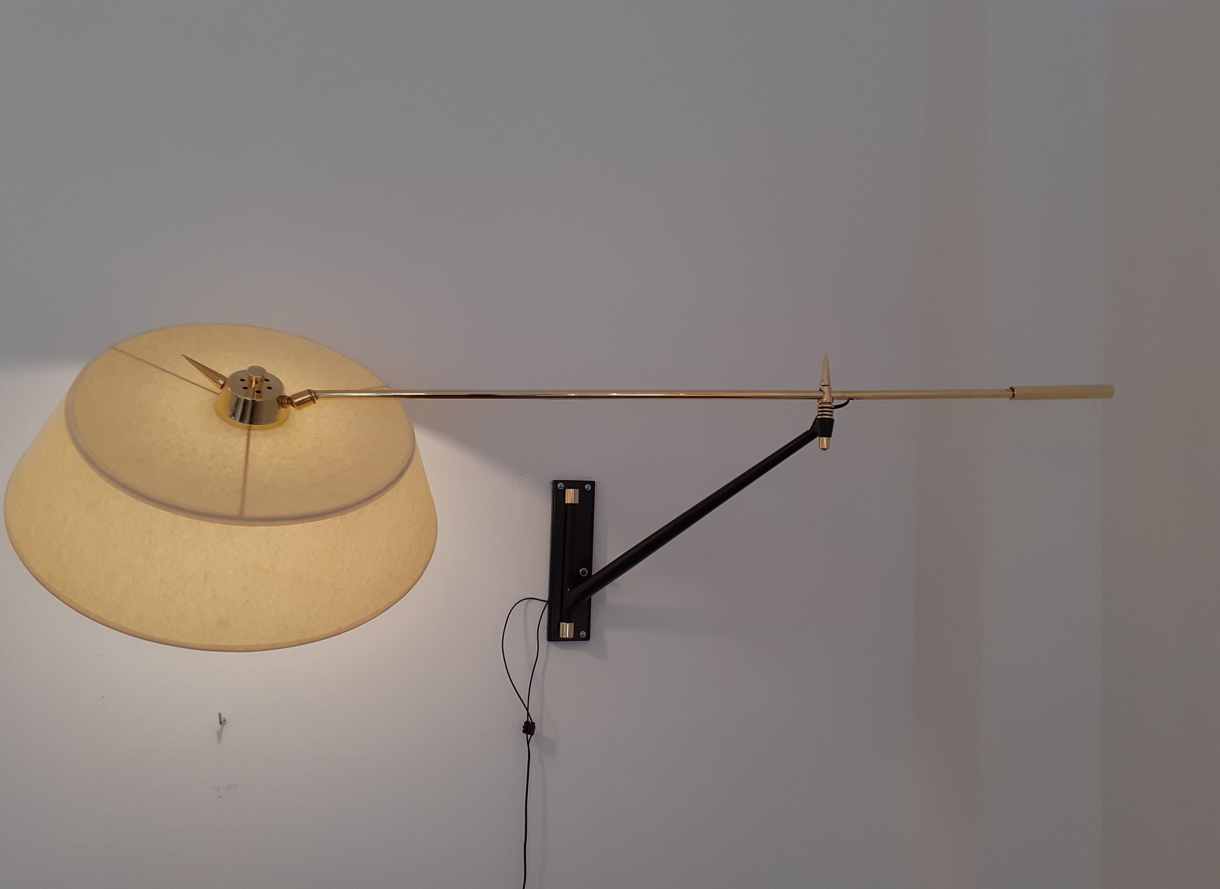 Brass wall lamp composed of a rectangular base in black lacquered metal on which is placed a swivel rod connected to an articulated brass arm.
A lampshade placed at the end of the arm, connected by a ball joint which allows the orientation of the