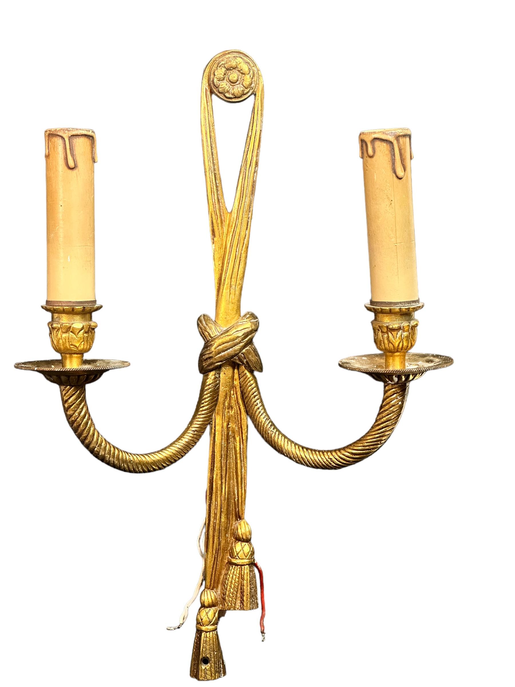 A nice sconce with 2 light sources, made of bronze with decoration of laurel branches, knot and tassels. The fixture requires two European E14 candelabra bulbs, each up to 40 watts. The wall light has a beautiful patina and gives each room an