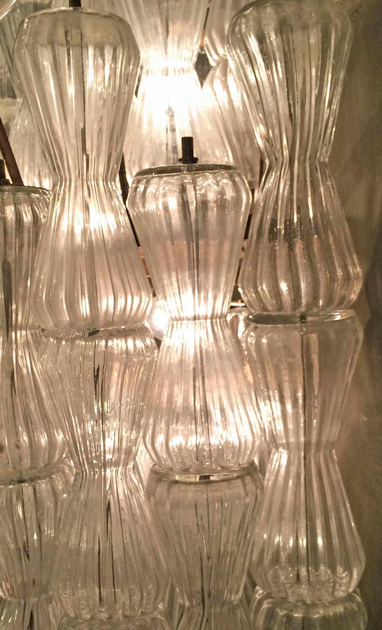 Single wall light made up of numerous strands of clear ribbed glass elements in an hourglass shape hung from a brass structure.
  
 