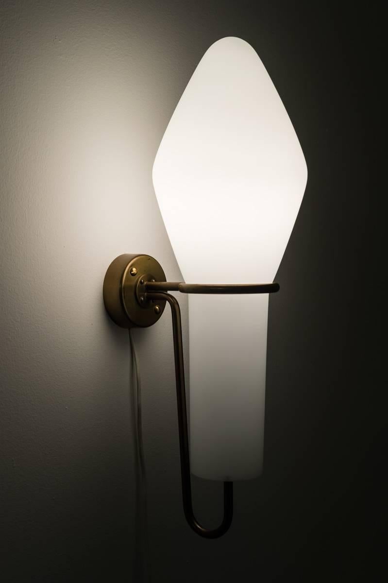 Very rare wall sconce by Hans-Agne Jakobsson. This lamp features one light source, hidden by a large opaline glass shade. The shade is held by a brushed brass frame with a smooth patina.
 