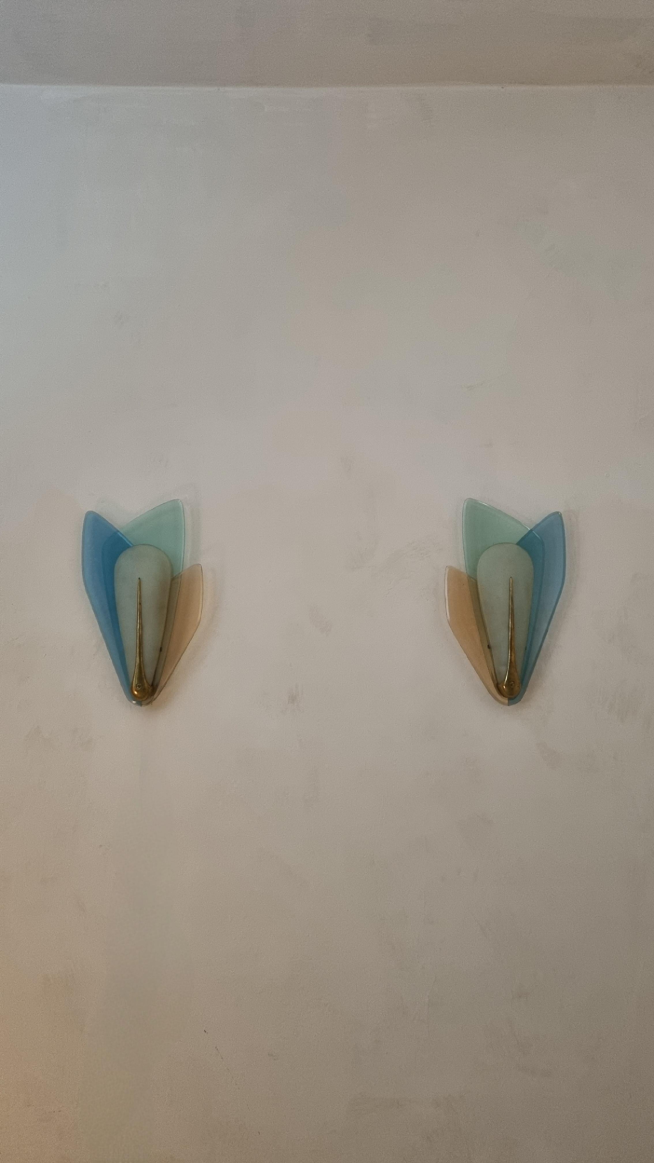 Iconiche lampade a parete disegnate da Max Ingrand per Fontana Arte nel 1960.
Struttura in ottone, cristalli colorati nei toni del blu, rosa e celeste, sagomati e diffusore in cristallo curvato satinato.

Celebre maestro del vetro d’arte, Max