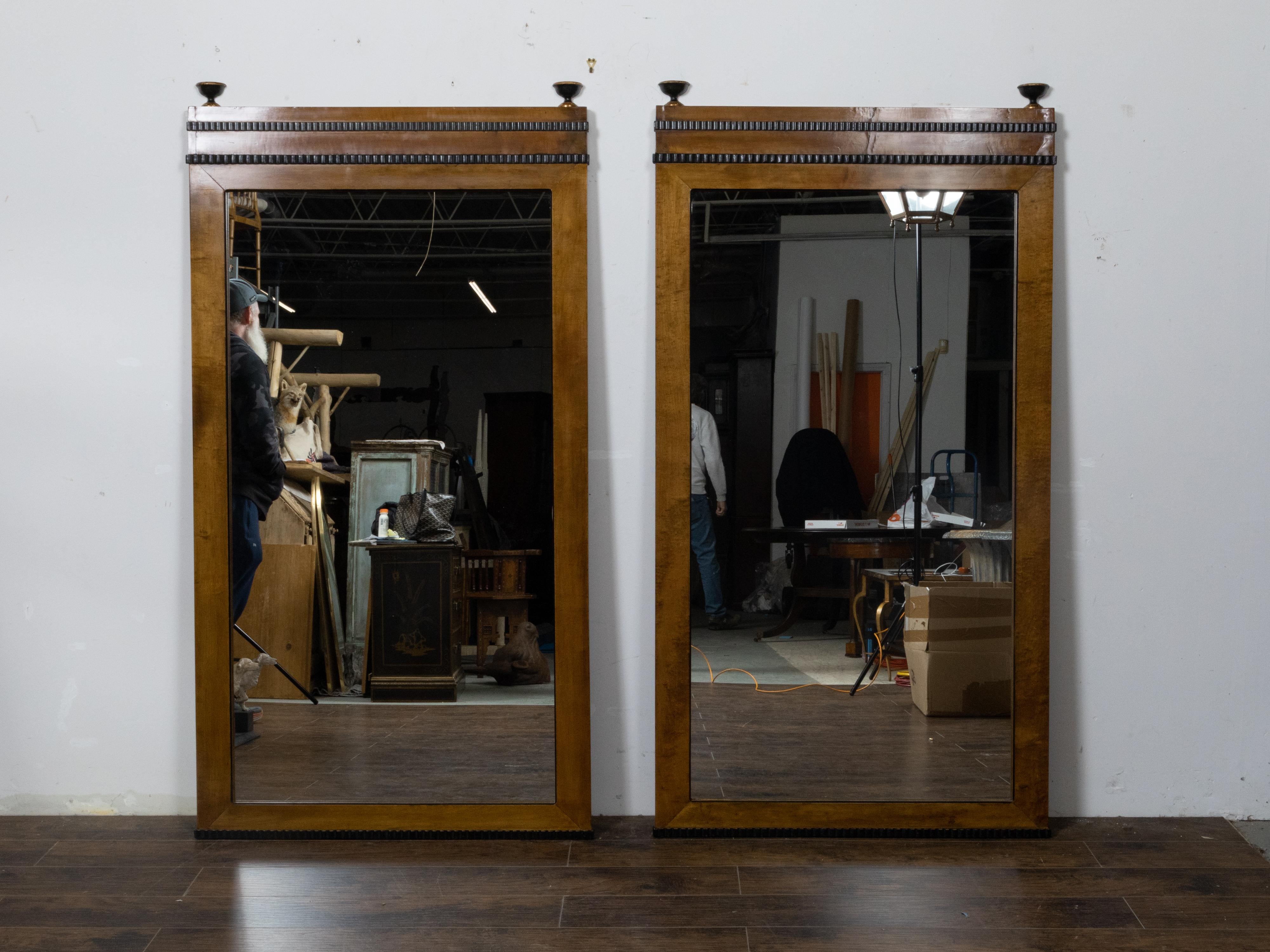 A pair of large Austrian walnut mirrors from the 19th century made of old Biedermeier components, with dark brown color, ebonized reeded motifs and turned finials with gilt accents at the top. These striking large Austrian Biedermeier mirrors