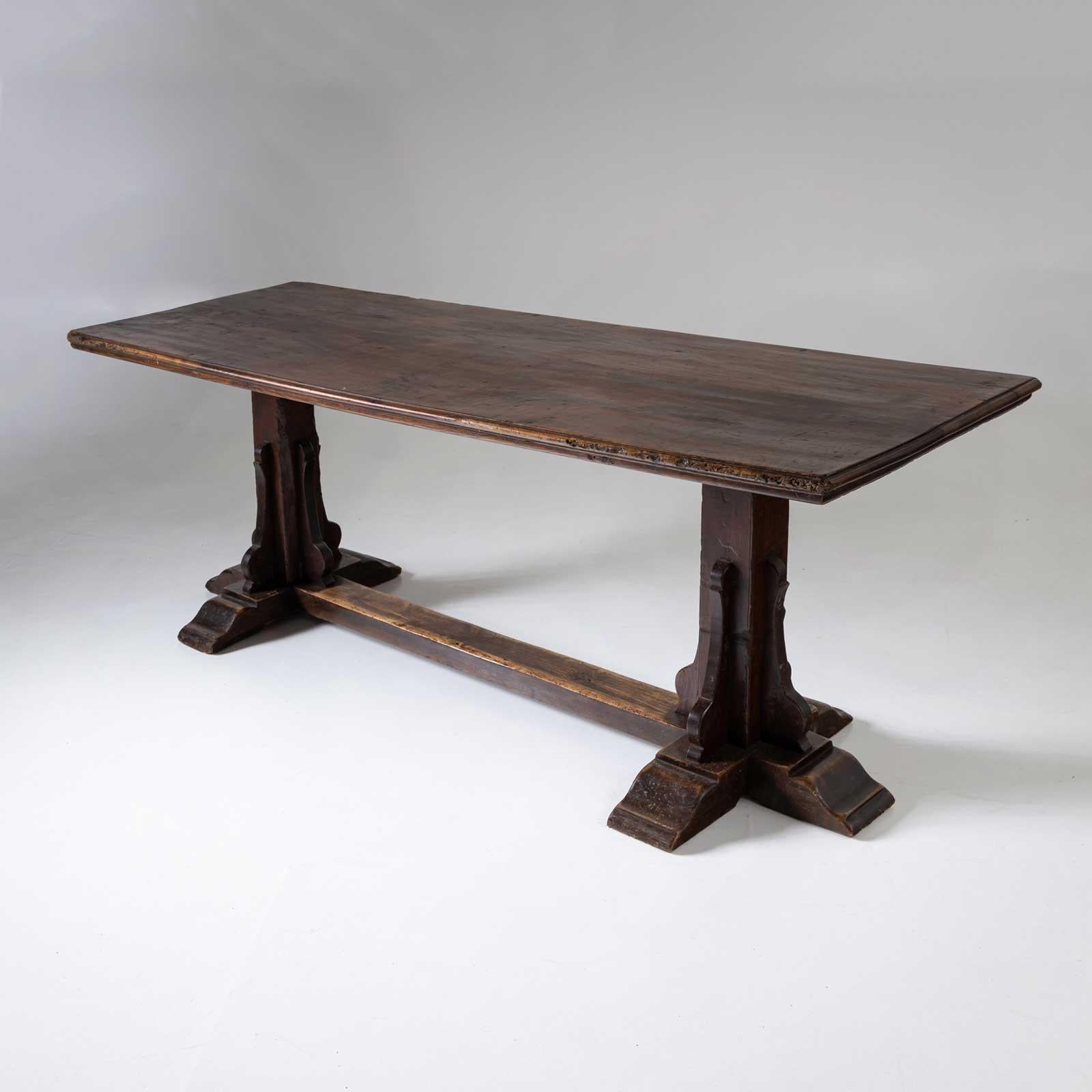 Grande table de salle à manger avec un plateau étroit et rectangulaire reposant sur deux pieds en colonne avec une entretoise intermédiaire. La table de réfectoire est en noyer et présente une belle patine.