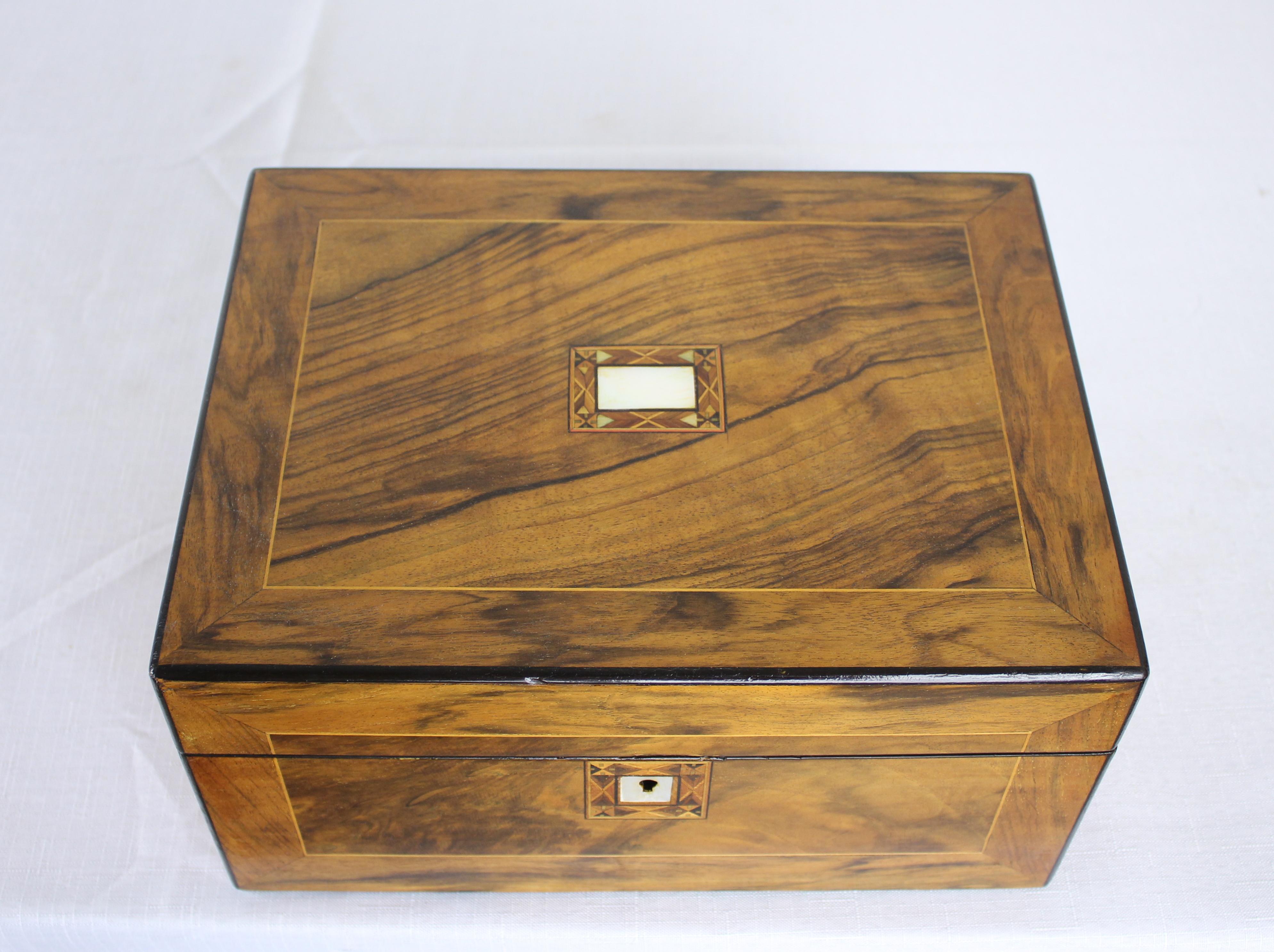A dramatically grained walnut sewing box inlaid with ebony and boxwood. Nice mother-of pearl detail around keyhole and on the top. Lined with vibrant pink satin. Original key and good divided interior space.