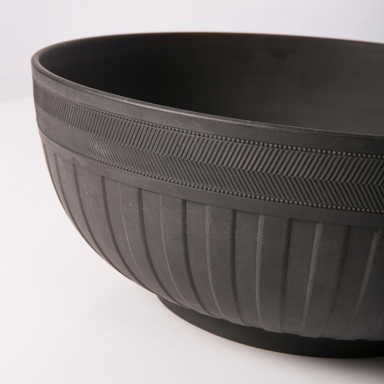 A large wedgwood black basalt engine turned bowl decorated around the outside with a simple band of chevrons at the top, and a band of wide vertical cuts below that. The vertical cuts are wide and deep enough that you can see the texture of the