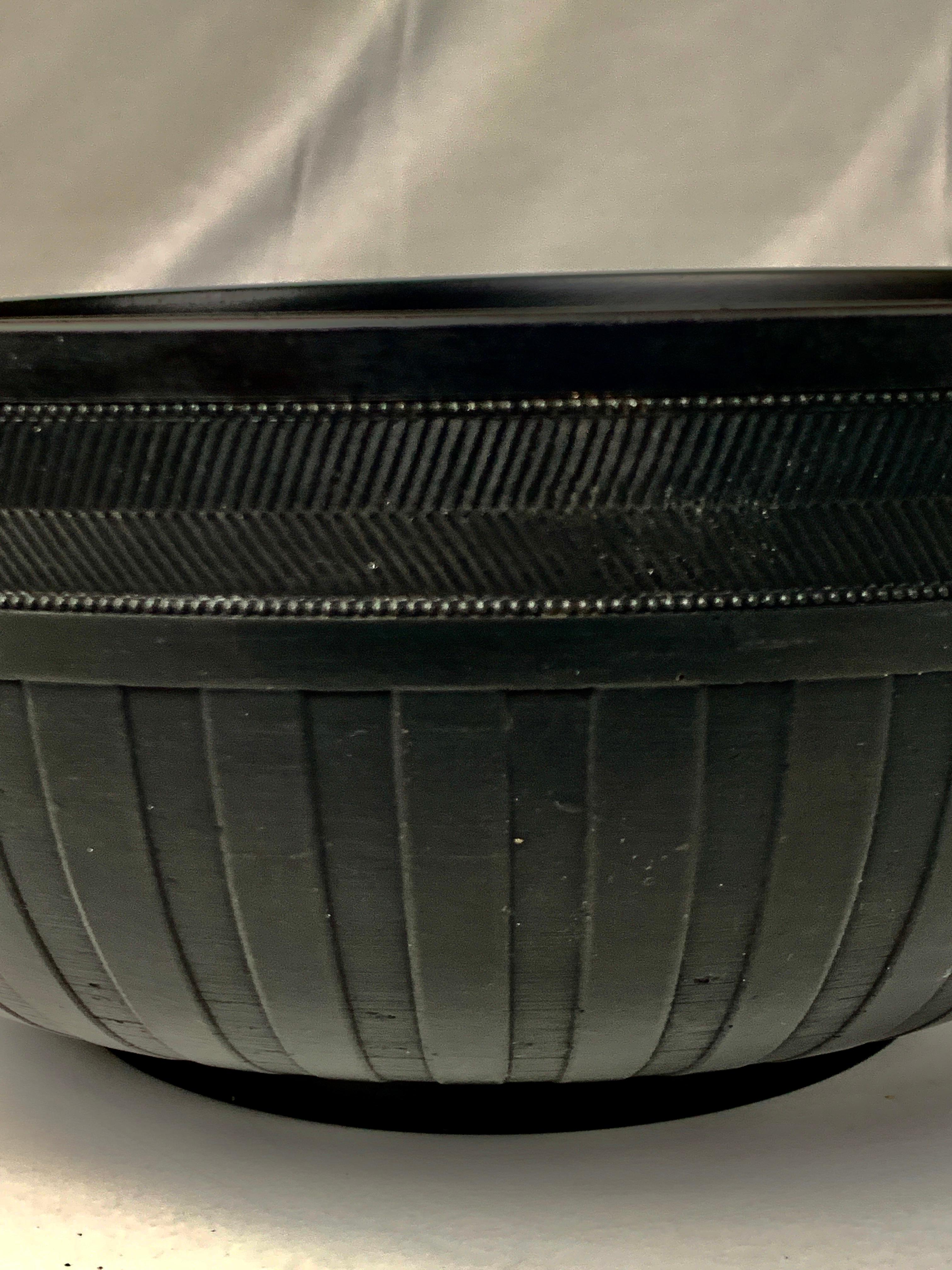 A large Wedgwood black basalt engine turned bowl decorated around the outside with a band of chevrons at the top and a band of broad vertical cuts below that. The verticle cuts reach all the way to the bottom of the bowl. They are deep enough that