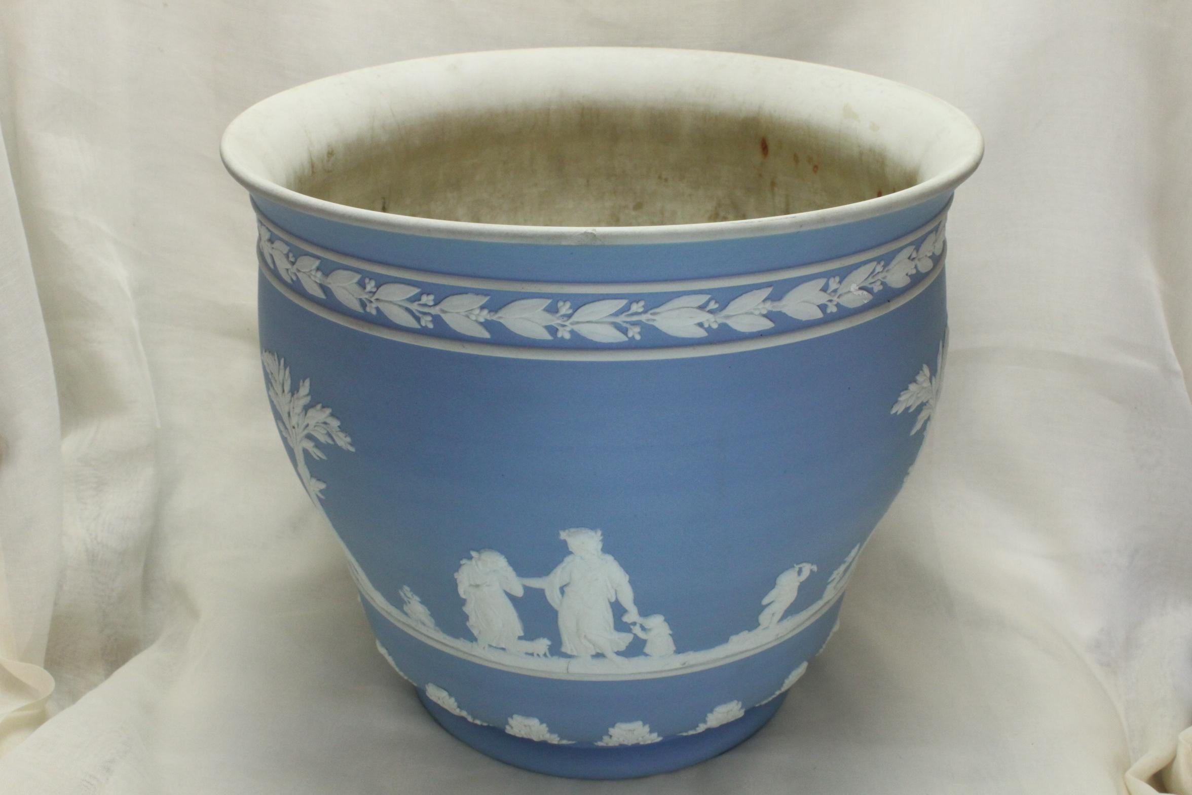 The body of this large Wedgwood jardiniere has been dipped in a light blue Jasperware and decorated with applied sprigs done in a white clay. The sprigs are made when clay is pressed into a very shallow mould, gently teased out, and then carefully