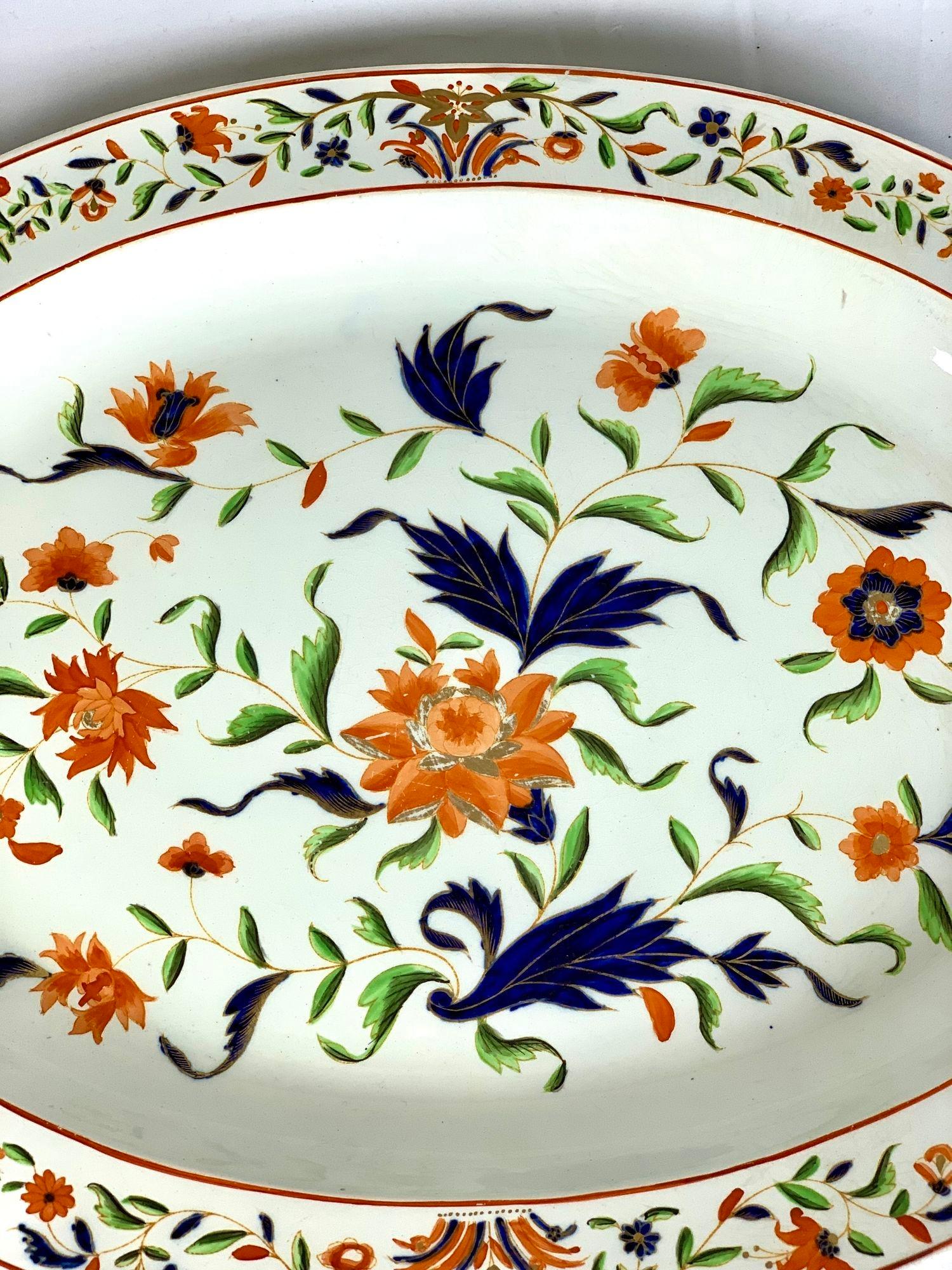 A large and lovely Wedgwood platter decorated with the Imari colors of orange and deep blue with accents of light green and gilt.
The colorful decoration depicts loose sprigs of leaves and flowers.
The border is decorated with a band of smaller