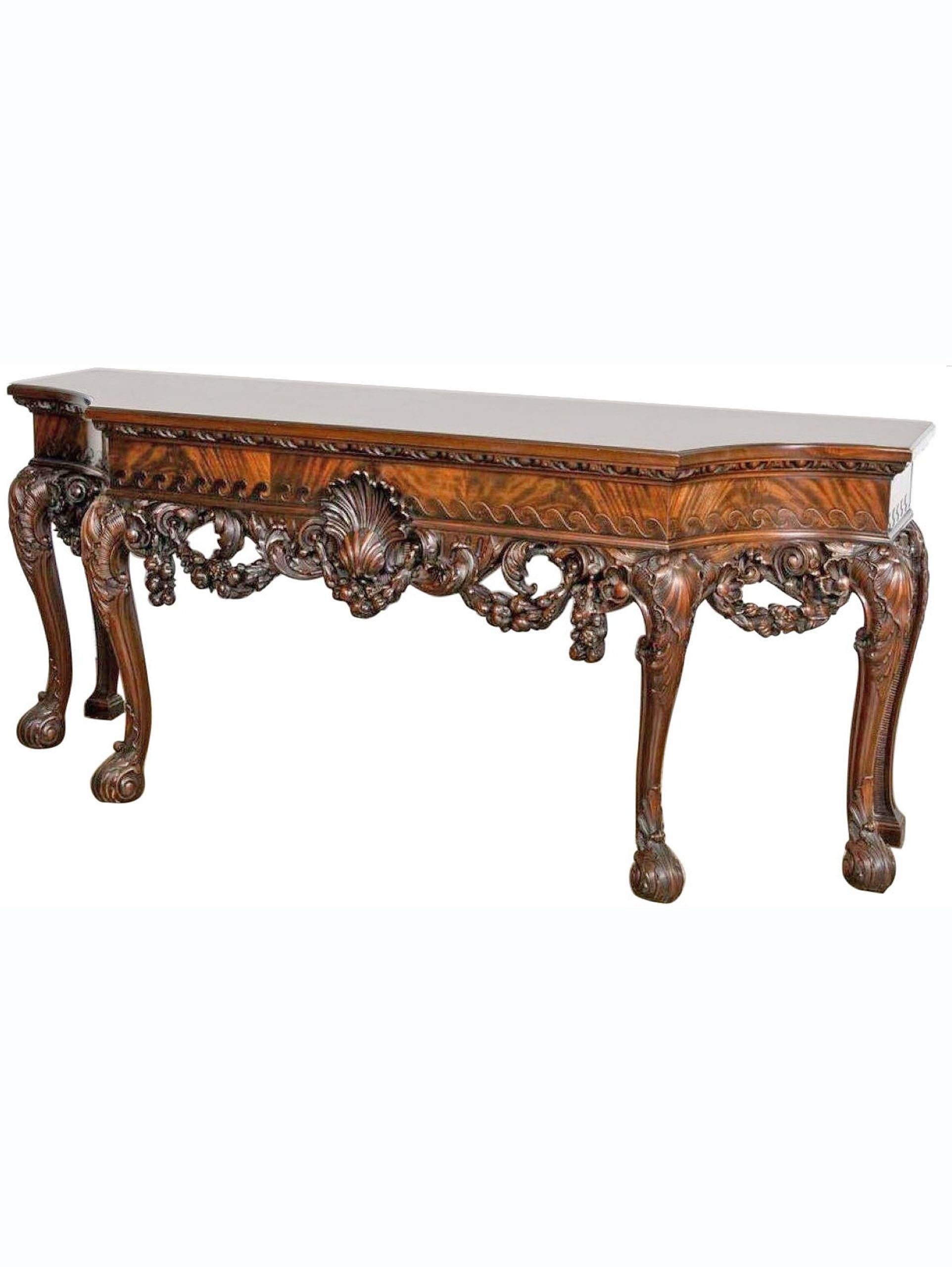 A Fine and well carved English mahogany console table in the George II style having a breakfront form with large scallop shell, the apron with floral and fruit swags, and rising on cabriole legs with acanthus decorated feet. England, circa