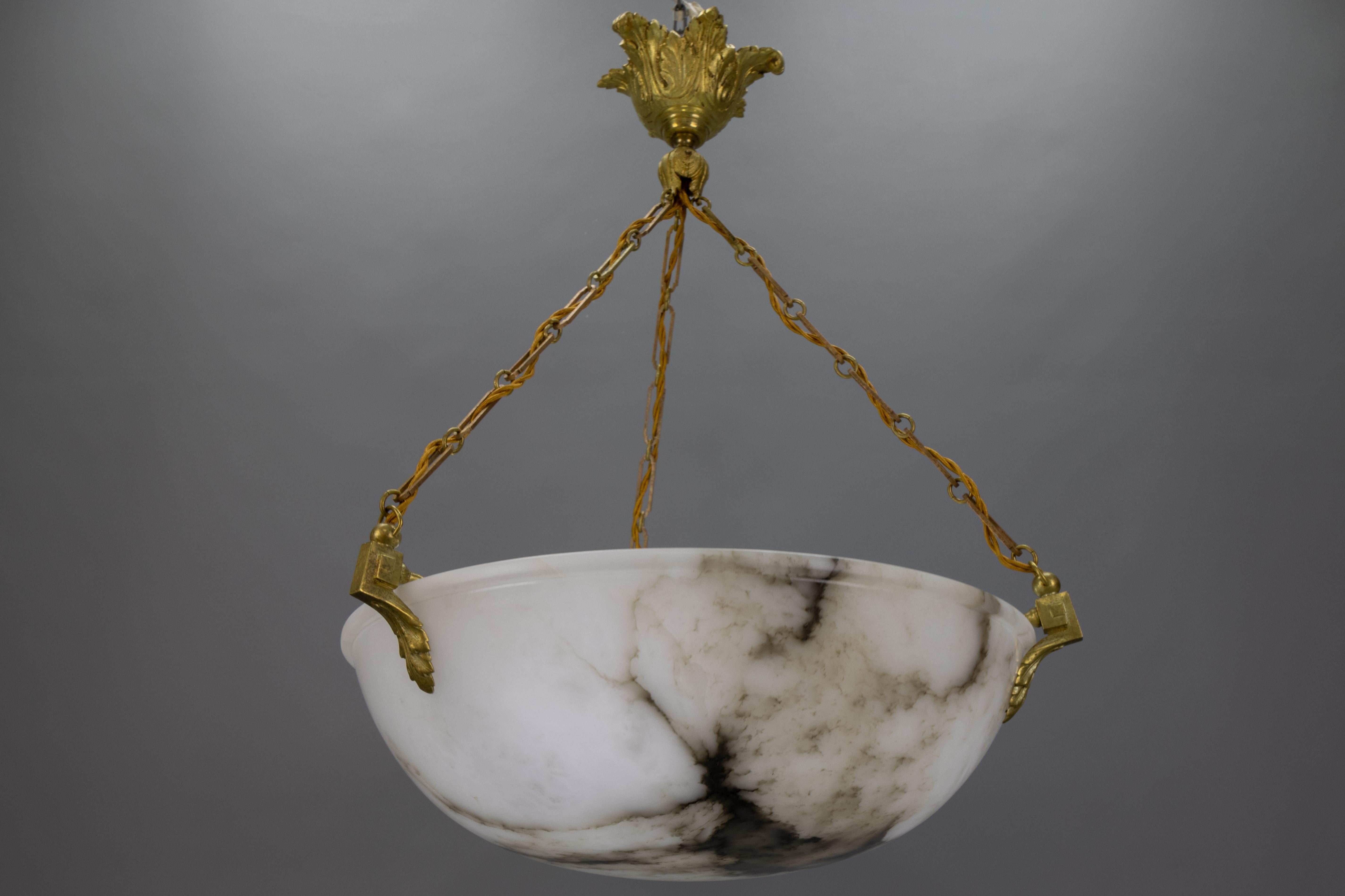 French Neoclassical-style pendant light made of black veined white alabaster with bronze fixtures. 
This stunning ceiling light fixture dates back to the 1920s. It features a beautifully veined white, large, and deep alabaster bowl suspended by