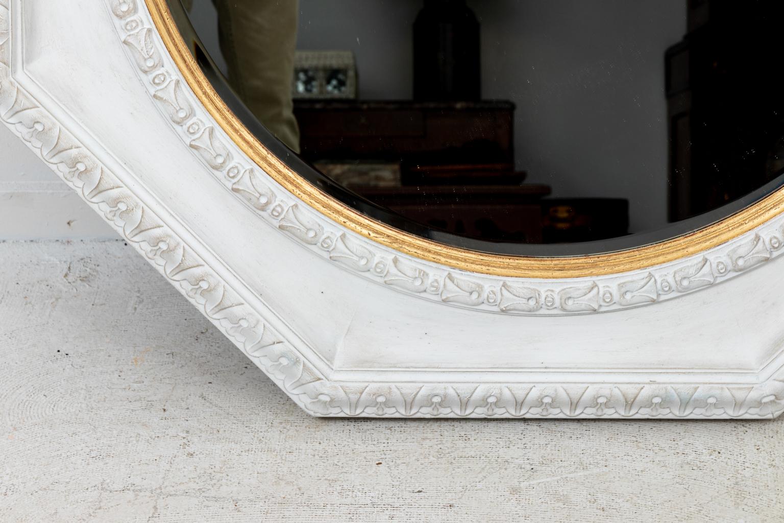 Hollywood Regency style large scale white and gold octagonal mirror with robustly carved bell flowers and moldings, circa 1980s. Made in the United States. Please note of wear consistent with age including some wear to the gilding on inner rim.