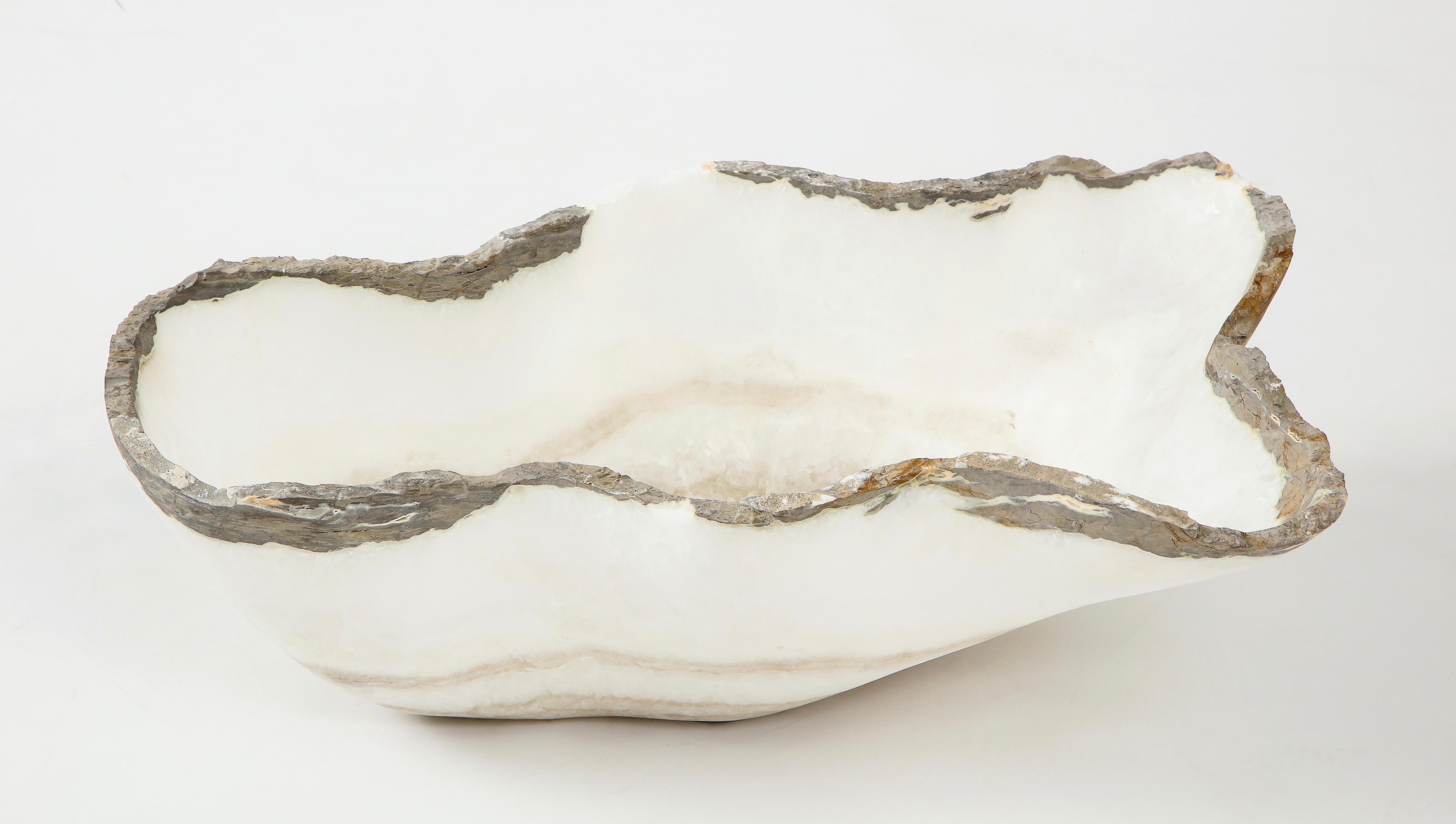 A large white and gray hand carved raw edge onyx bowl or centerpiece in an impressive size. The dark gray edge provides a dramatic contrast with the Stark white calcite body banded with lighter gray rings towards the bottom. Utilitarian and
