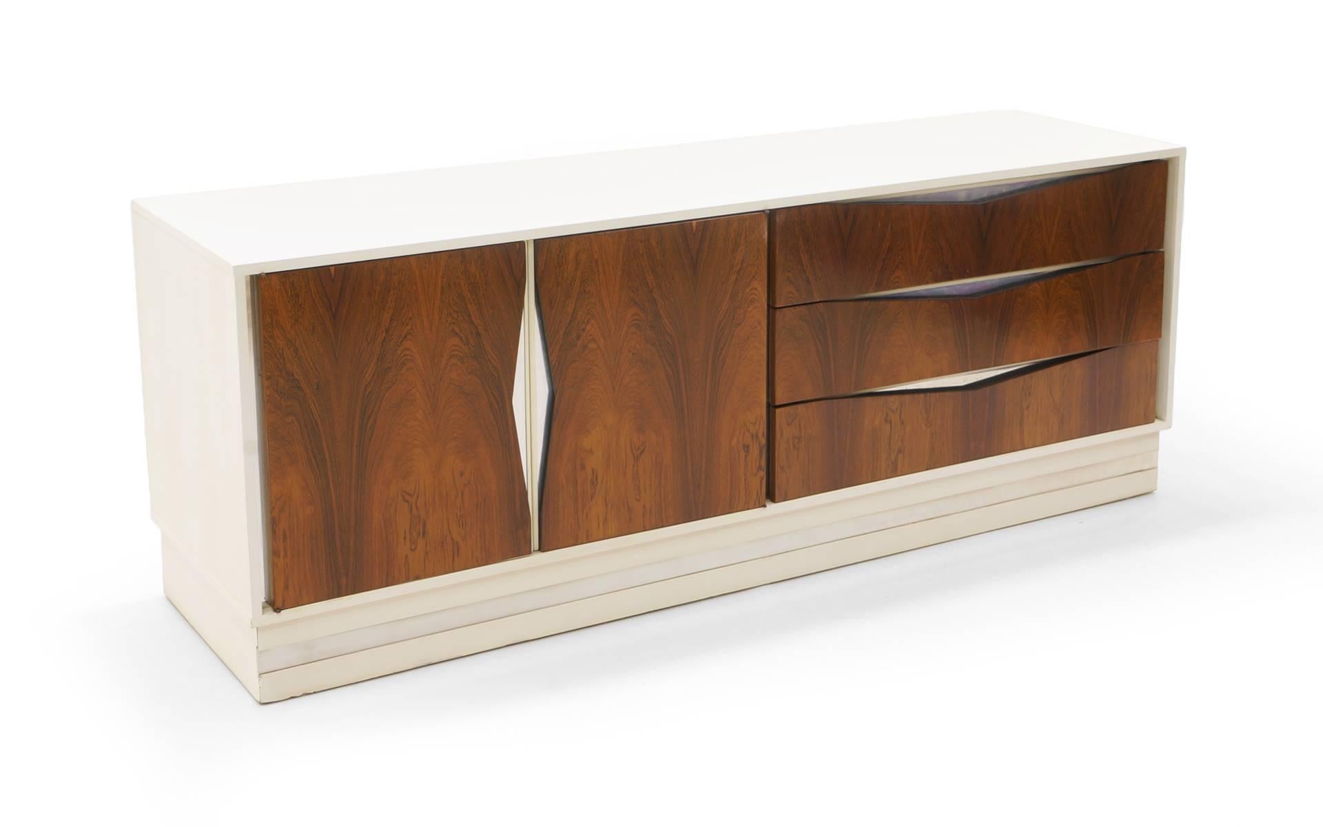 Striking white lacquered and Brazilian rosewood dresser with chrome accents. Seven feet long. Three drawers on one side and two doors on the other revealing another three large drawers. We also have a listing for the matching nightstands. All have