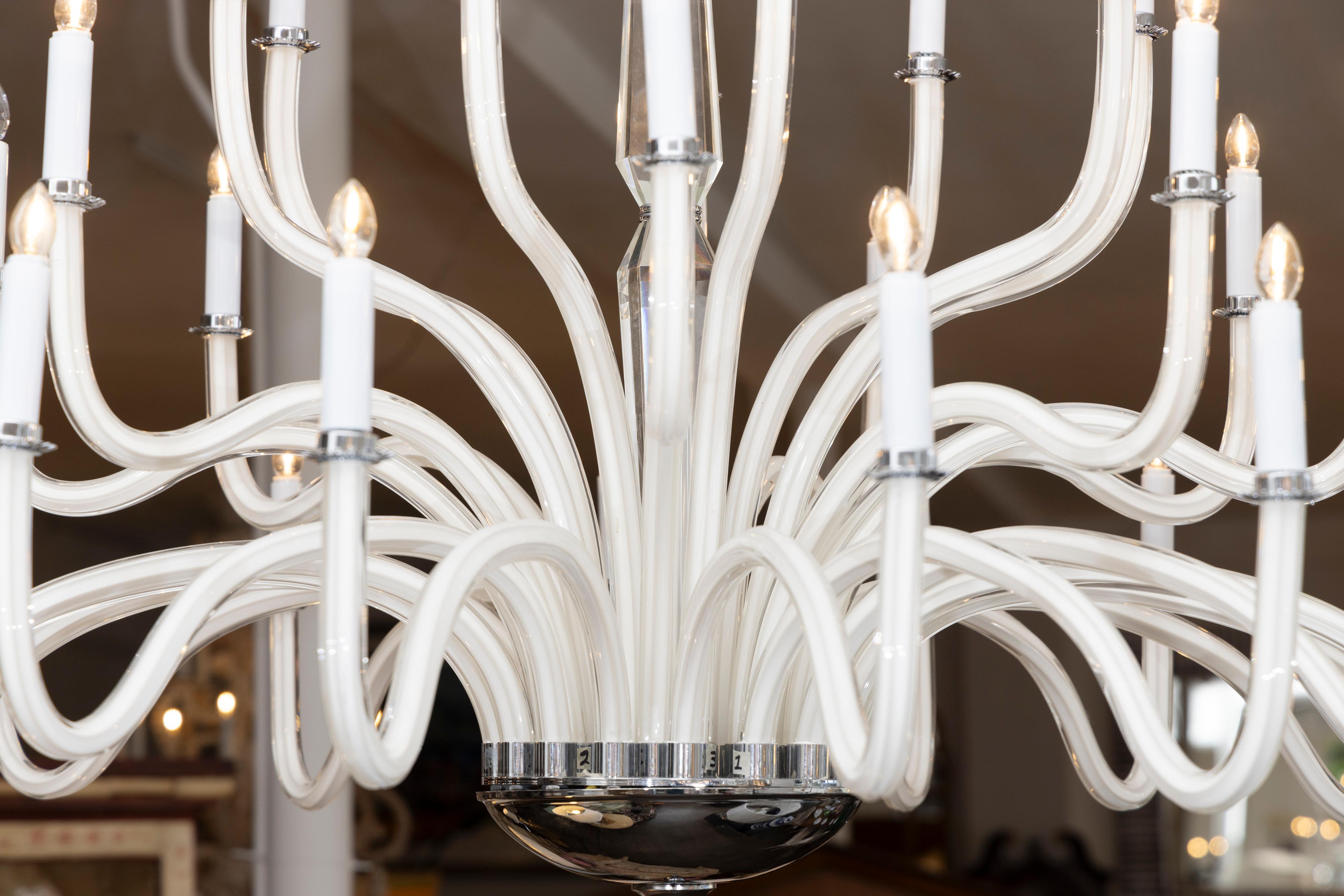 This is a stunning contemporary white glass 32-light chandelier with polished chrome bobeches centered by a glass-clad column.  The bottom section contains a polished chrome cap.  