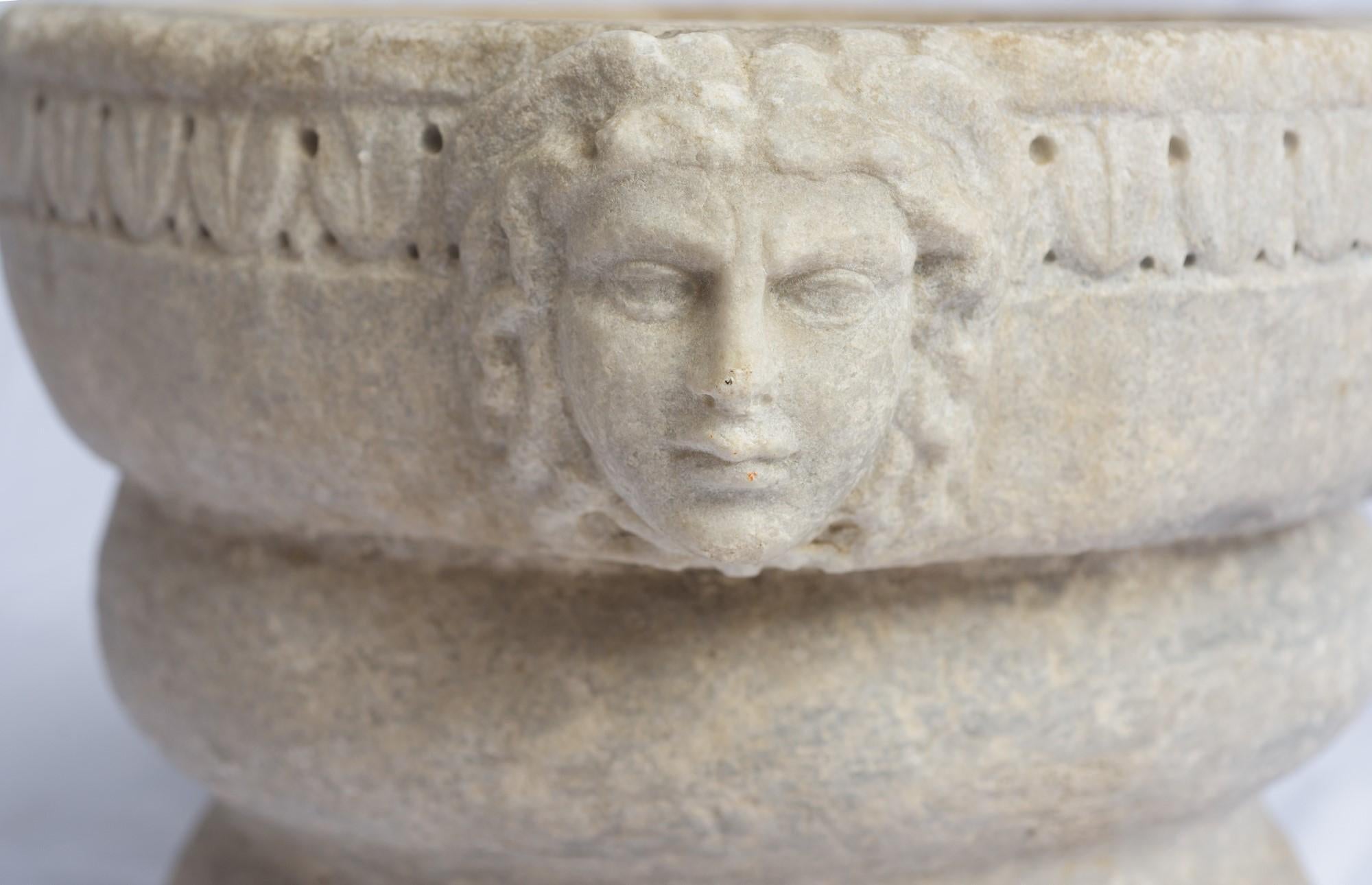 Un très grand et unique mortier en marbre blanc du XVIe siècle avec des mascarons latéraux sculptés. 
Les mascarons sont des éléments architecturaux décoratifs qui se présentent sous la forme d'un visage ou d'une tête sculptée, représentant souvent