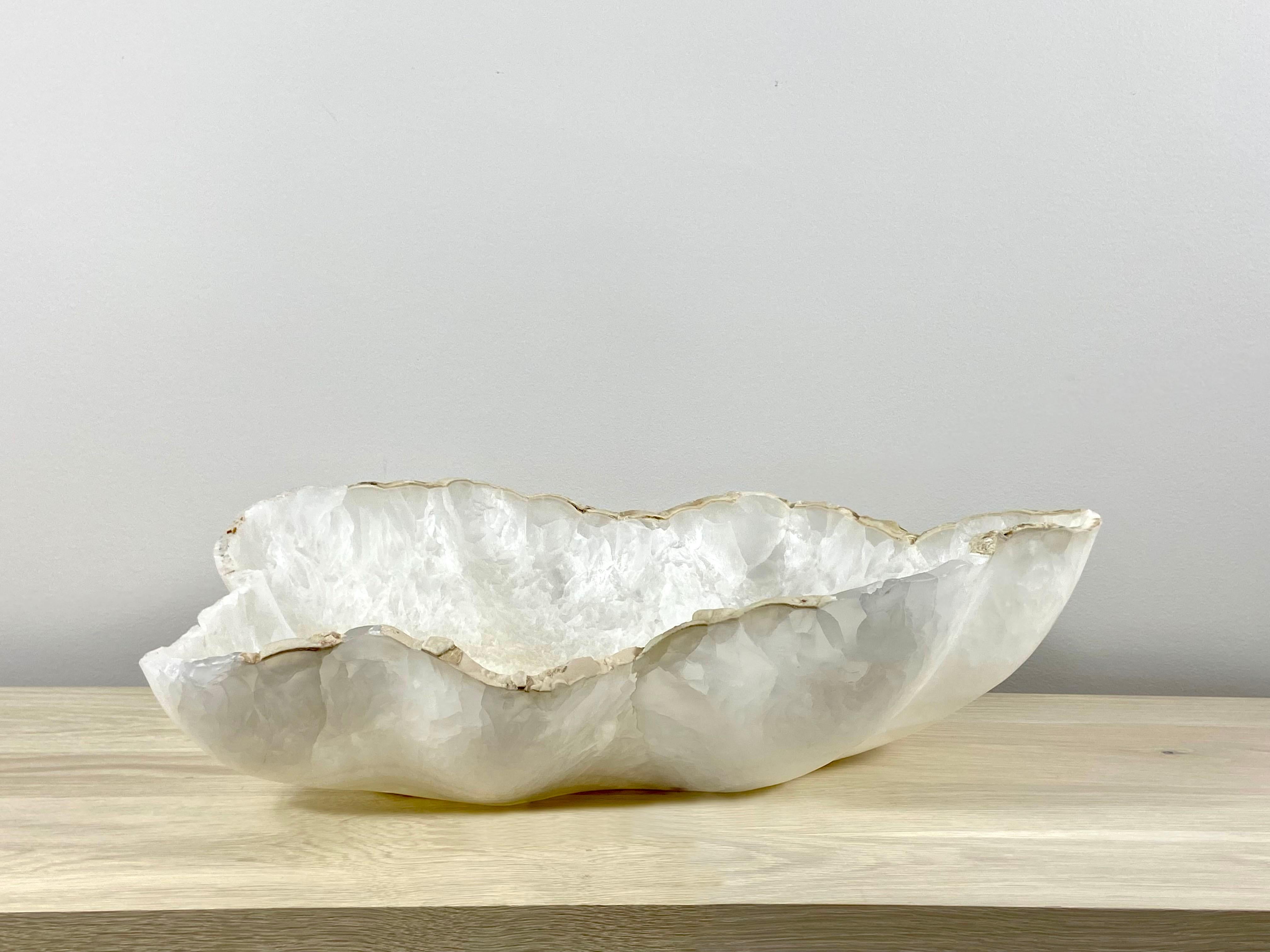 A stunning large white onyx bowl with a raw edge. This one of a kind decorative bowl is meticulously hand-carved from a single piece of onyx by skilled artists to reveal its' inherent characteristics. This beautiful bowl is a perfect sculptural