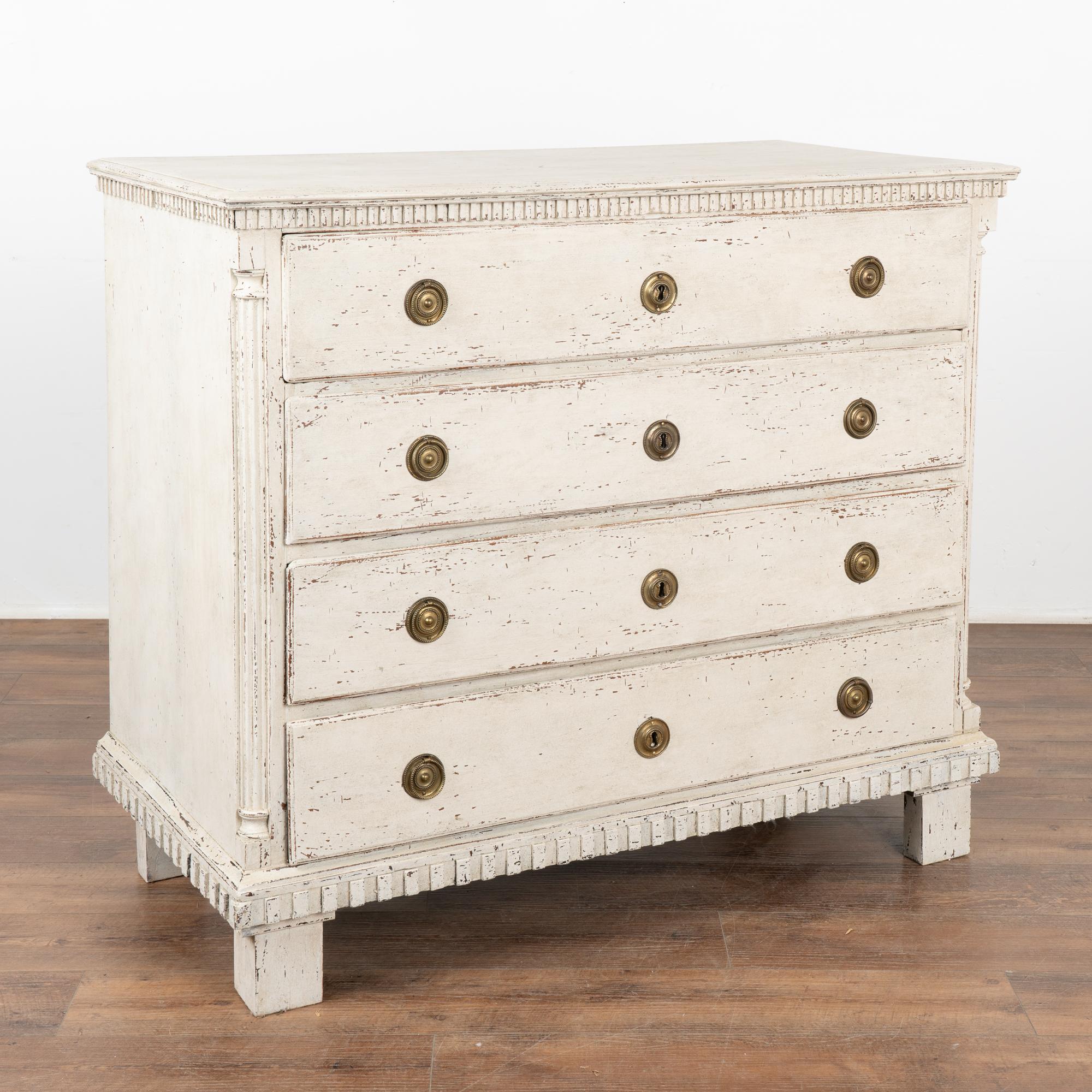 Lovely oak chest of four drawers with dentil molding carved along top and skirt with fluted half columns along canted sides.
The newer, professionally applied antique white painted layered finish adds a touch of grace that fits the age of this large