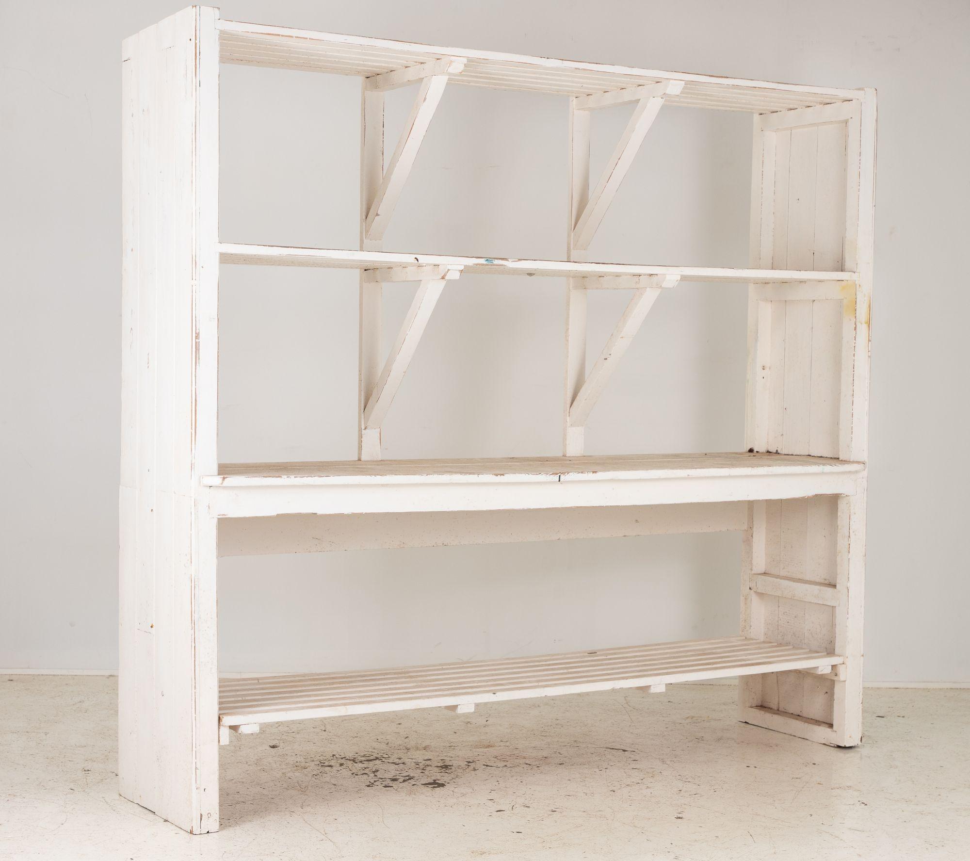 Esta estantería a gran escala de la Floristería, pintada de blanco, es un complemento versátil y rústico para cualquier espacio. Cuenta con dos estantes fijos de gran altura para expositores grandes, y la parte superior de la unidad sirve como zona