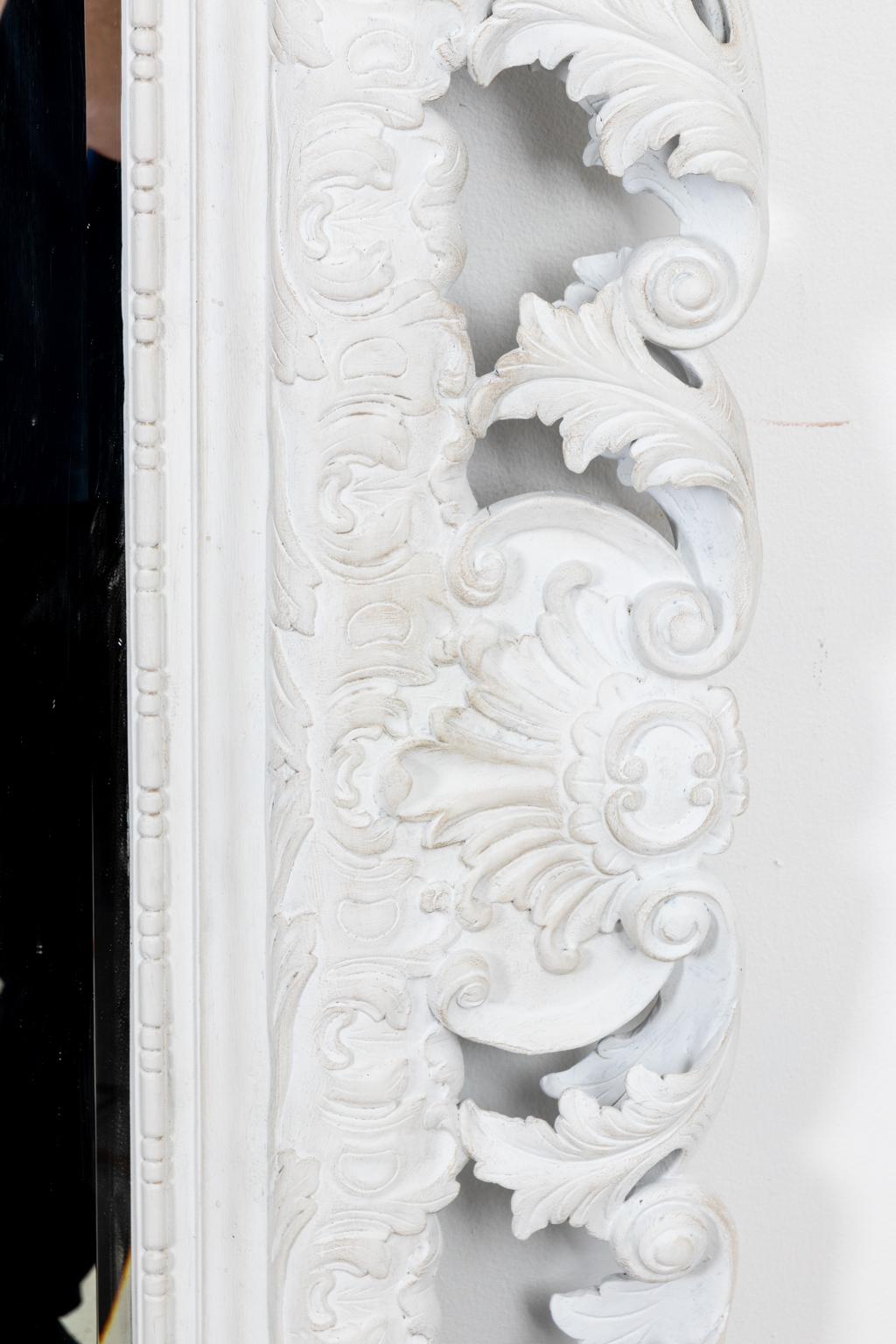 Circa 1980s robustly carved and white painted Rococo style mirror with scrolled foliage detail on the frame. Newly painted in a chalky white and over scaled at 4' by 5 '. Please note of wear consistent with age including minor chips and scuffs. The