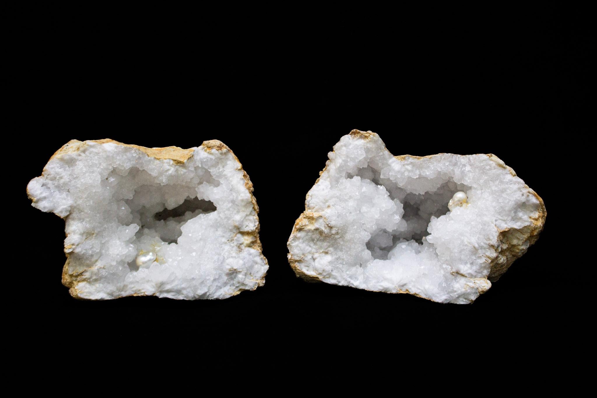 Large white crystal quartz geode split into two halves each with a large naturally forming baroque pearl.

Geodes are formed as gas bubbles within volcanic lava. Over time, the lava flow weathers away to leave the quartz geode buried deep in the