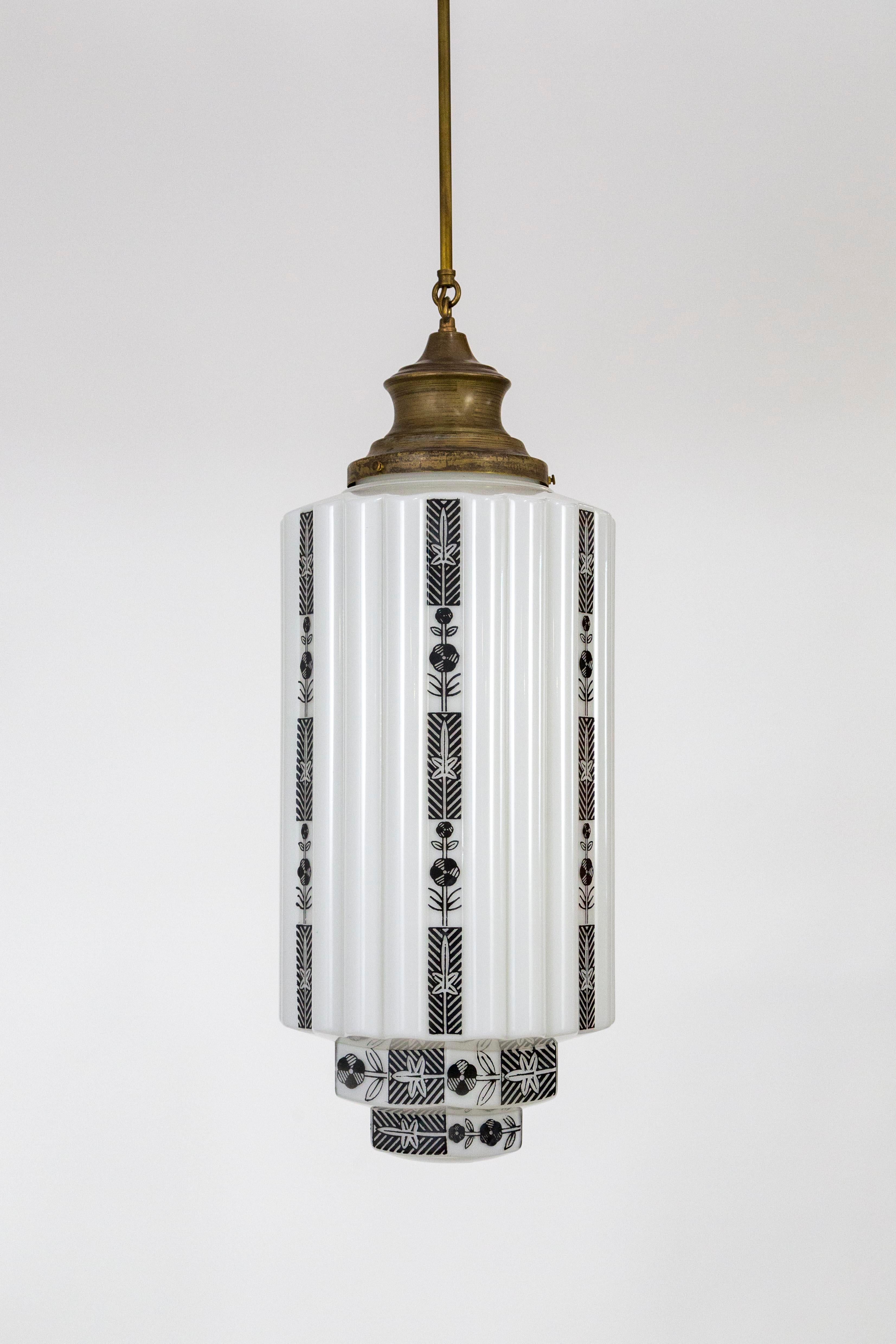 A large, white, ribbed, skyscraper pendant light with vertical black flower motif stripes, stenciled on white glass. An Art Deco design of the 1930s; newly made with antique glass. Hangs from a long, slender, bronze tinted, brass stem and shade