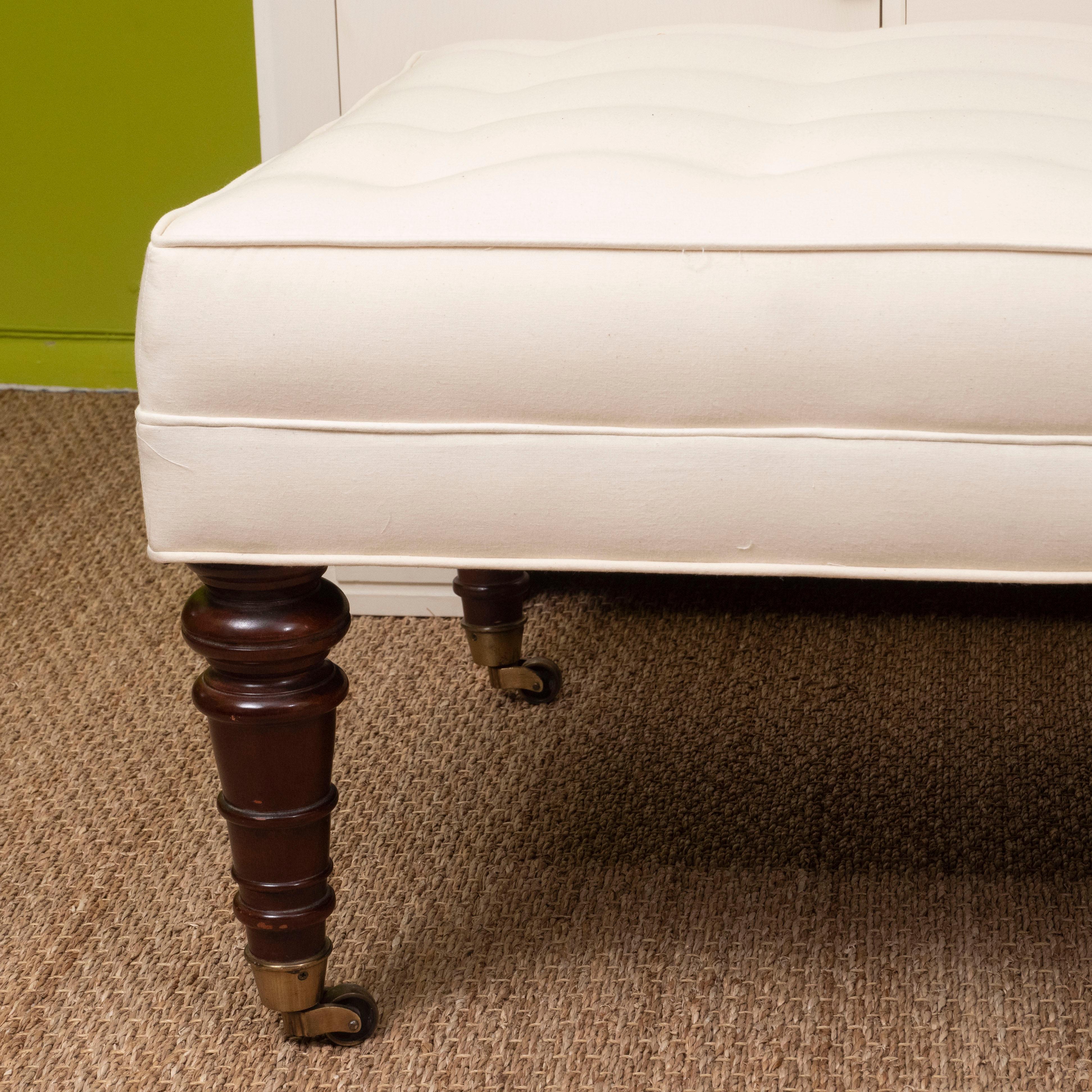 A large, tailored white ottoman with button tufting on turned wood legs with castors. It's clean lines make it perfect as an ottoman or coffee table in traditional or contemporary spaces.