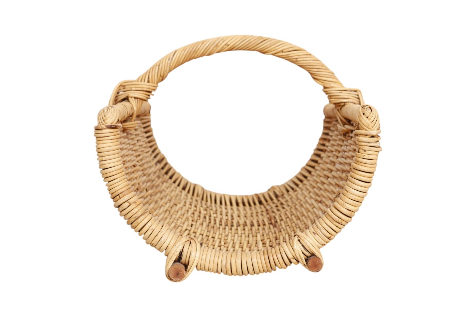 Un grand panier de cheminée en osier tressé pour contenir le bois de chauffage. Fabriqué en rotin avec un cadre en bambou. Le rotin torsadé forme une poignée fixée par une jonction en T tressée, et en dessous se trouvent deux longs pieds en bambou.
