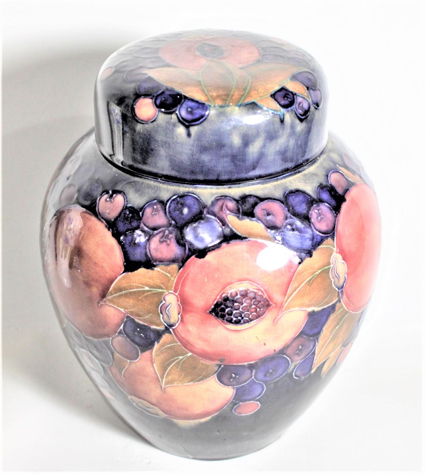 This large lidded ginger jar was made by the Moorcroft Pottery company of England in circa 1935 with the pomegranate patterned glaze. This art pottery lidded jar is done with a deep cobalt blue ground with a series of pomegranates and berries around