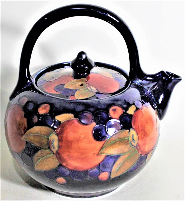 This large art pottery teapot was done by the Moorcroft Pottery company of England in circa 1925 in their 'Pomagranite' pattern. The teapot is done using the signature Moorcroft cobalt blue ground, with a series of fruit around the outside, and