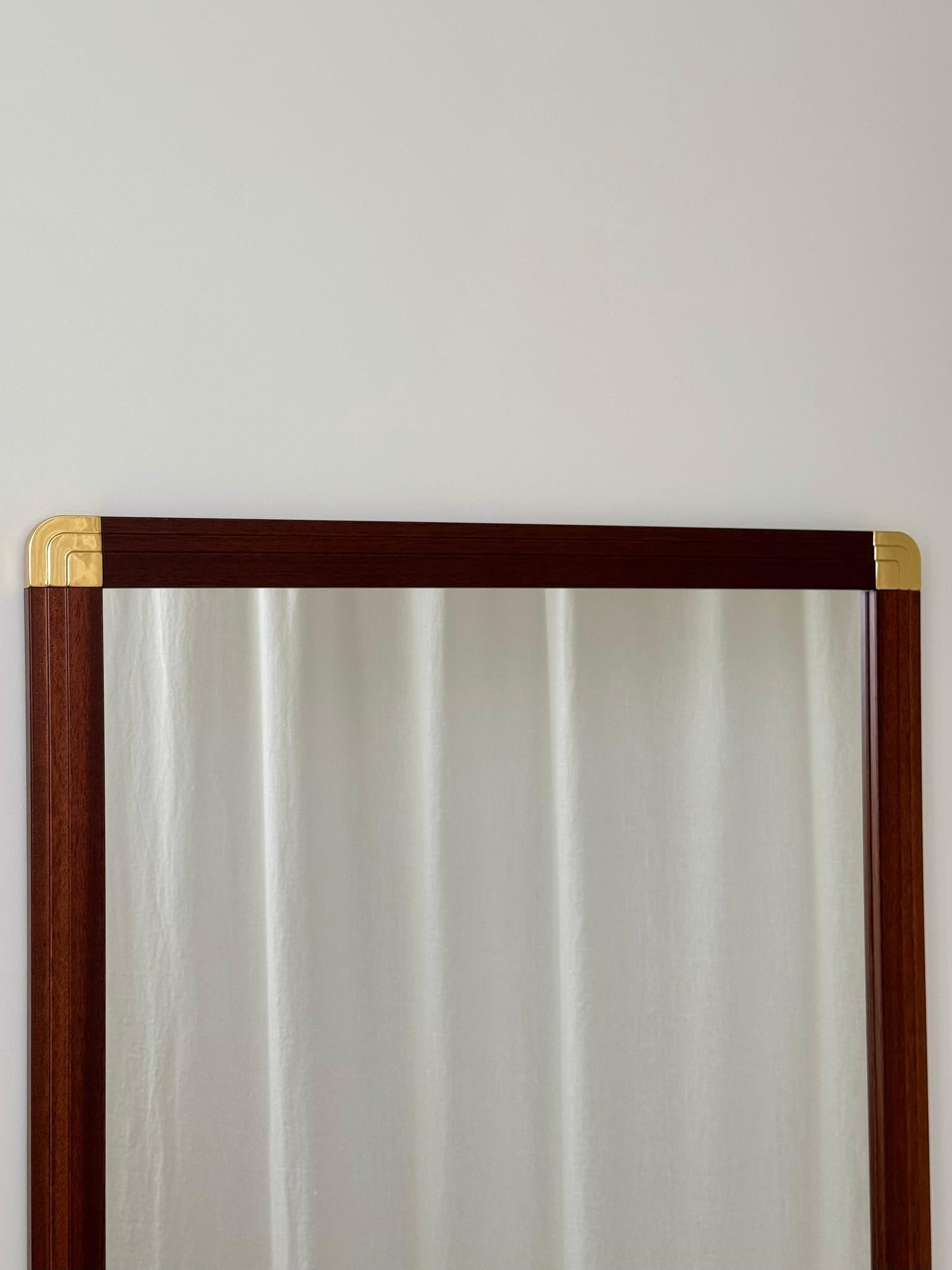 Un gran espejo de pared de madera con esquinas decorativas de latón. Buen estado vintage. Cristal transparente con un pequeño arañazo hacia la base (visible en la cuarta y quinta imagen). Listo para colgar.