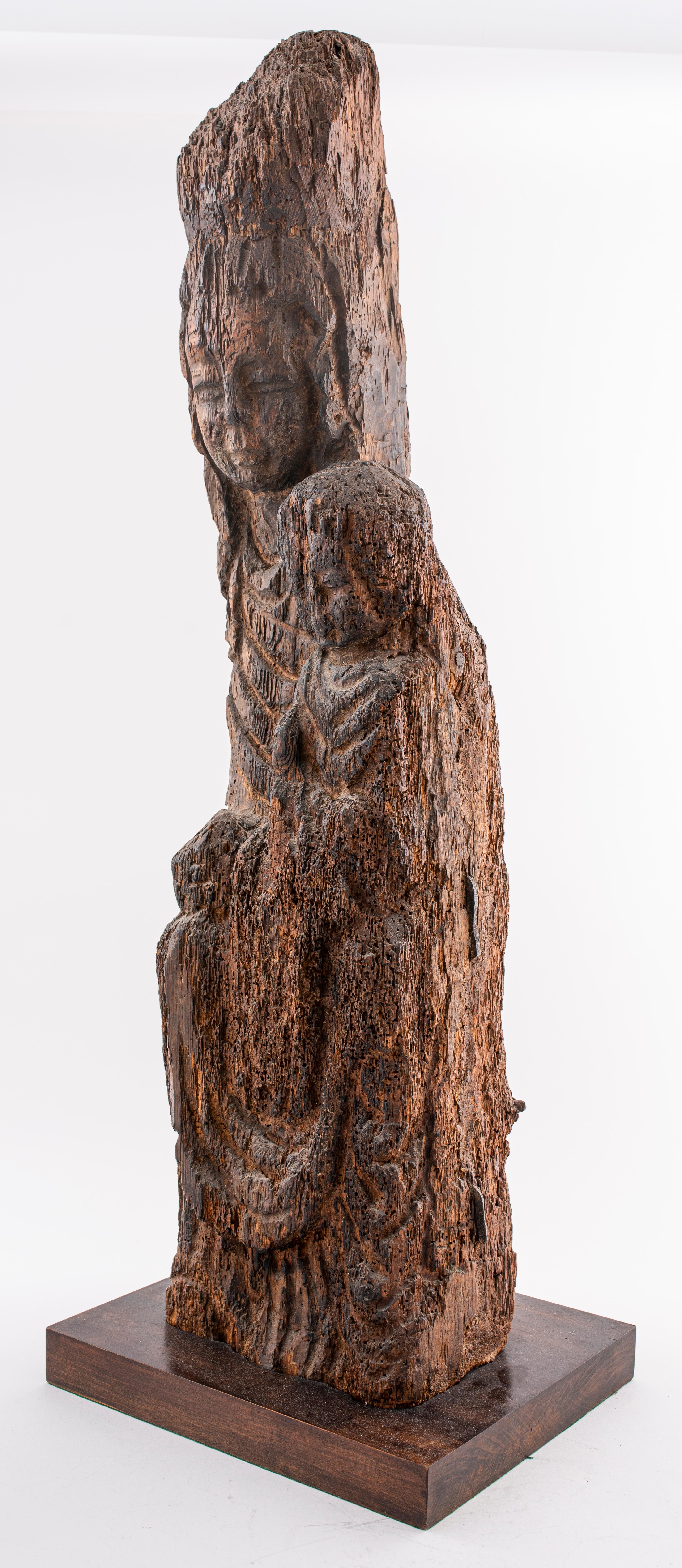 Large wooden figure of Kuan Yin / Guanyin, Buddhist Madonna, the goddess shown seated with a child on her left knee, her hair in a high topknot under a cowled headdress and her long robes falling in folds to the base, roughly hew from one block of
