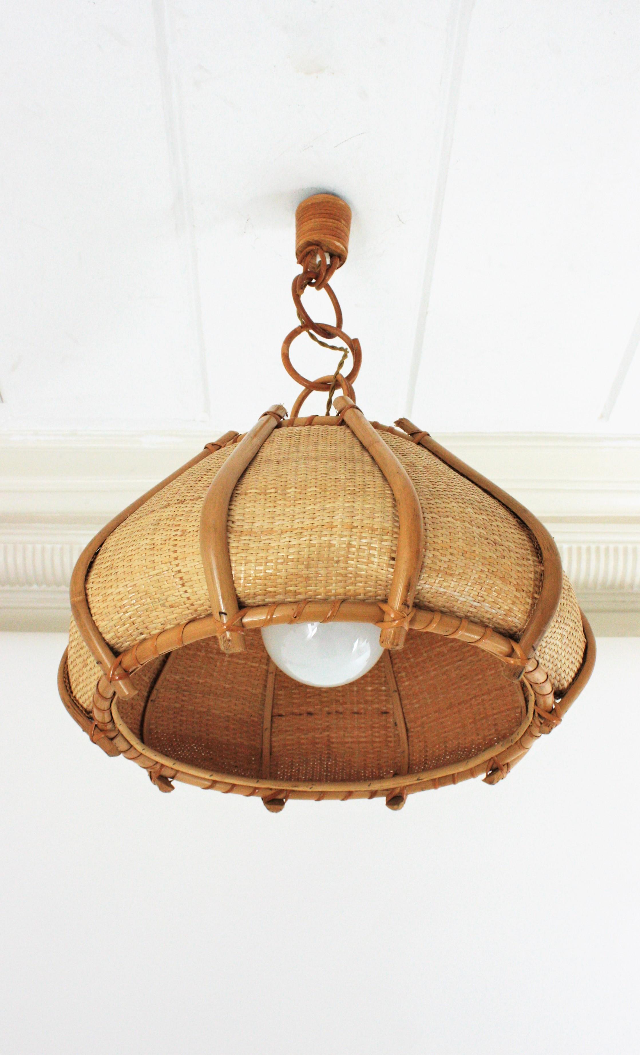 Mid-Century Modern woven wicker and bamboo large bell pendant / hanging light. Spain, 1960s.
This beautiful suspension lamp features a bamboo and wicker wire bell shaped shade with bamboo decorative vertical bars. It hangs from a chain with large