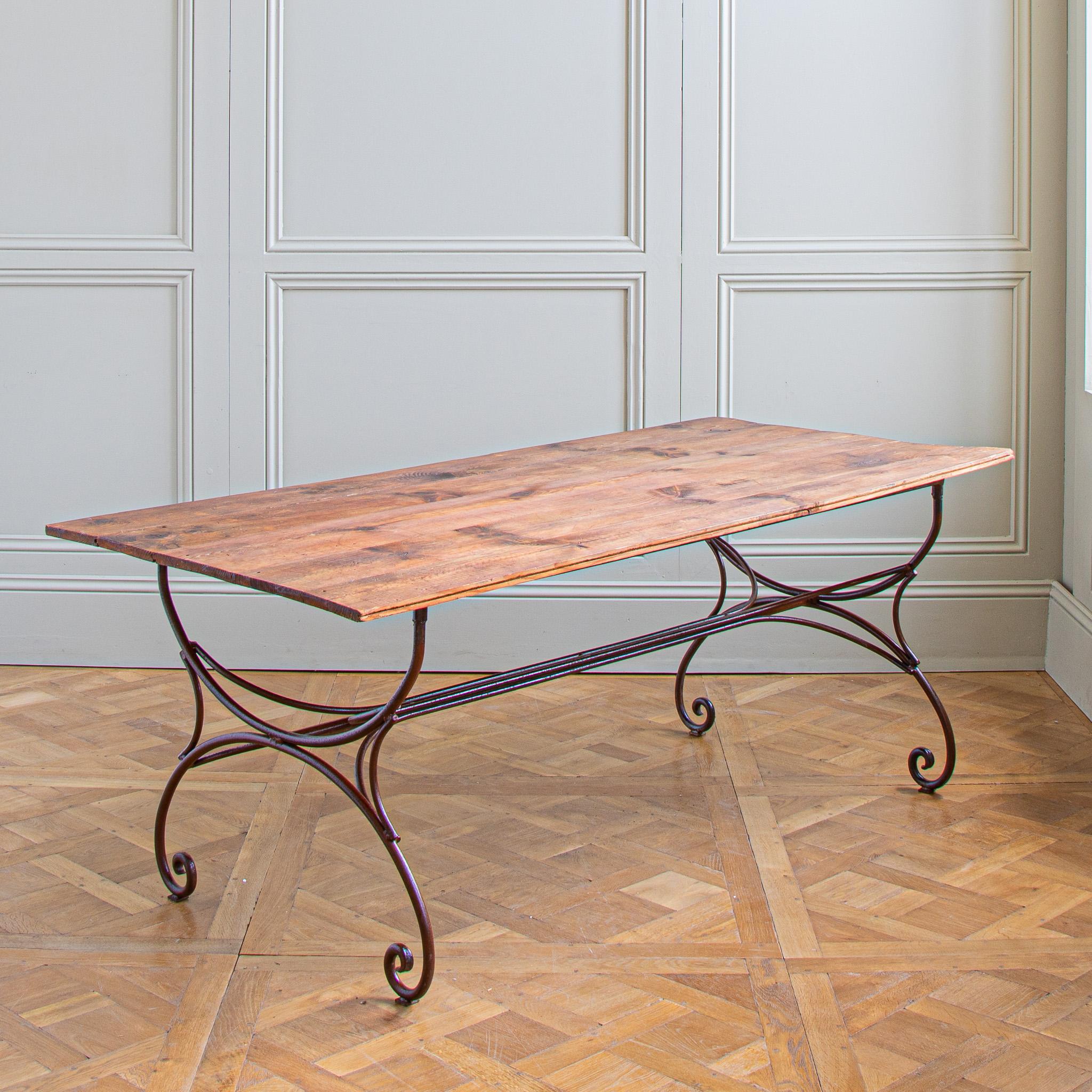 A large, mid century, rustic table from the South of France which can be used indoors or out. The wrought iron base has a deep, age-oxidised, reddish hue which has been polished and sealed to preserve. The curved base of hand-worked lines looks