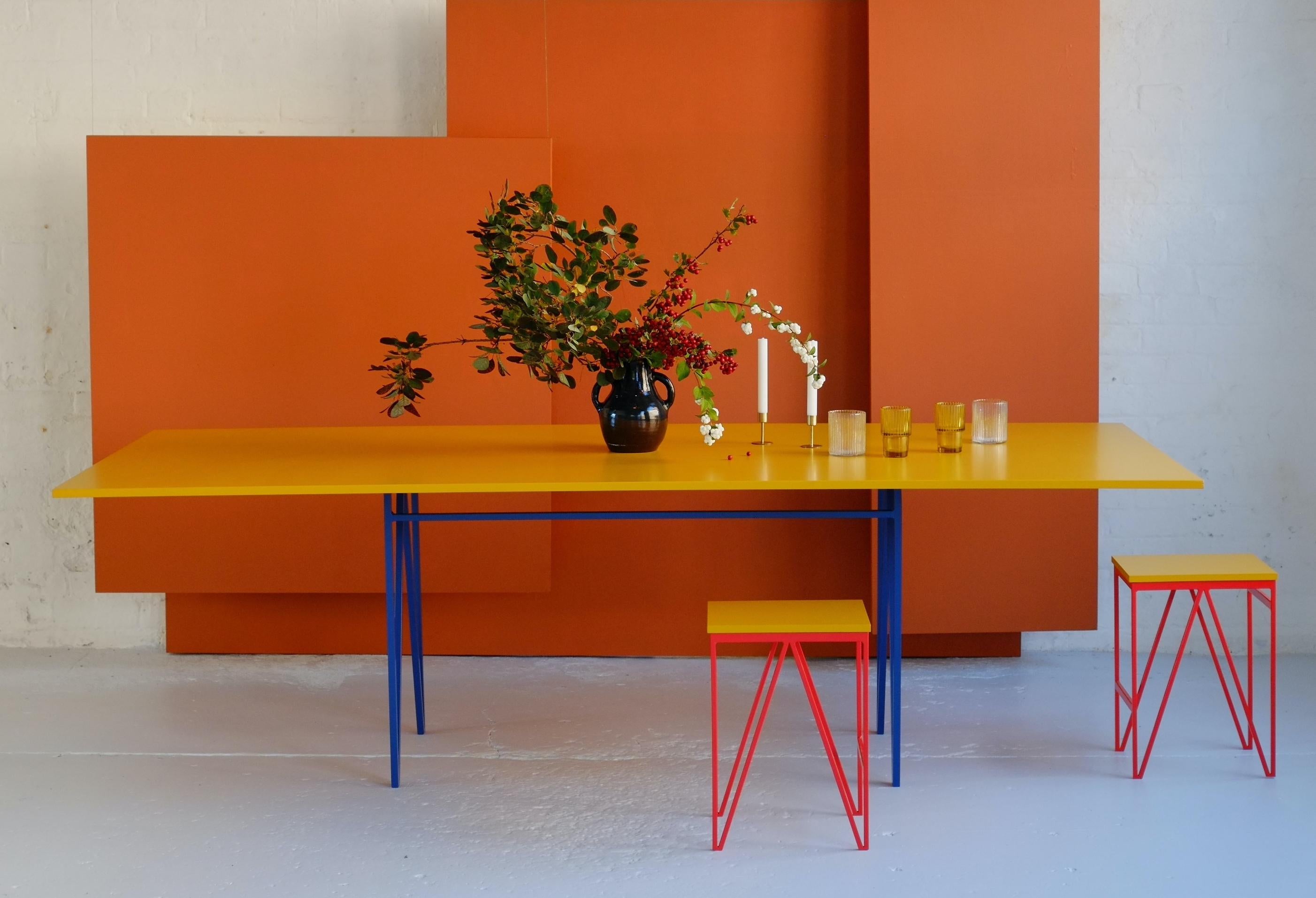 Cette table de salle à manger Colour Play est fabriquée avec des pieds en acier solide recouverts d'une couche de poudre de bleuet et un plateau laqué jaune foncé contrastant. Le plateau de la table est recouvert d'une laque alimentaire appliquée