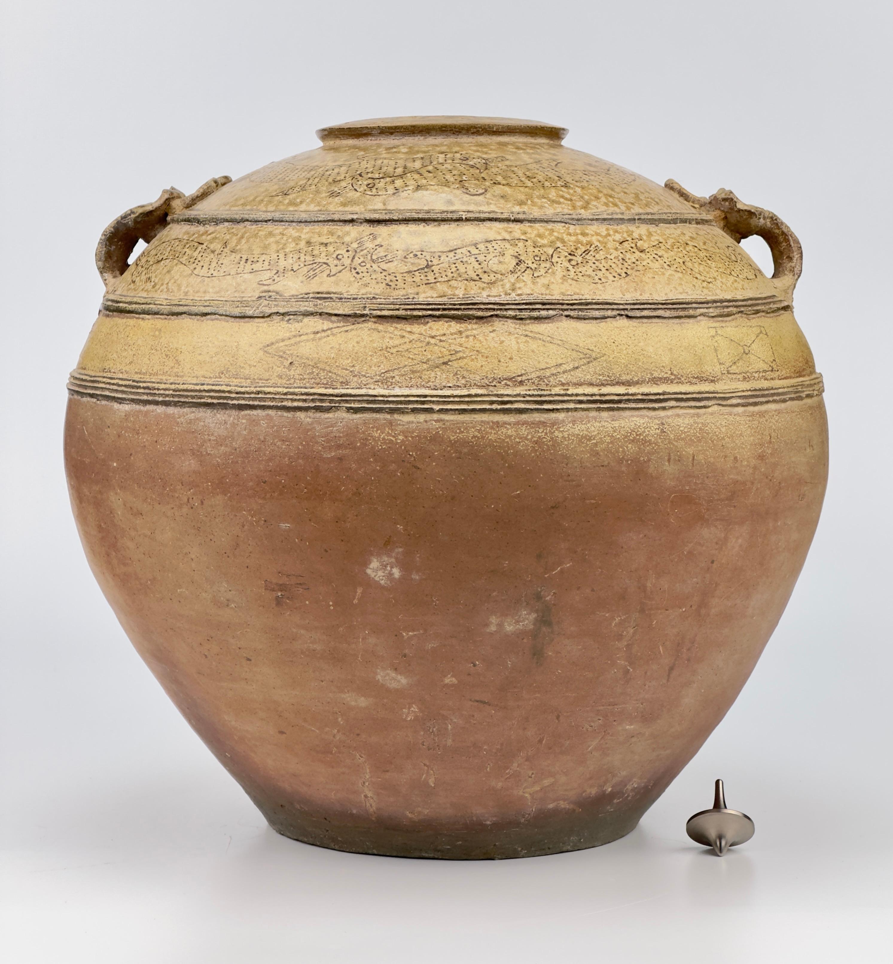 Robustly crafted with a voluminous spherical body and a layered mouth rim, this jar features a pair of taotie handles. It is adorned with three horizontal bands on the upper half of the olive-green-glazed body, which segment the glazed area into