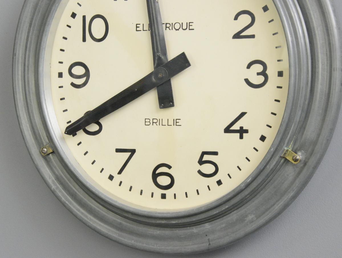 Large zinc wall clock by Brillie, circa 1930s

- Zinc casing with brass hinges
- Steel dial with ivory dial and black numbers
- Glass face
- Original hands
- New AA battery powered quartz motor
- Made by Brillie
- French, 1930s
- Measures: