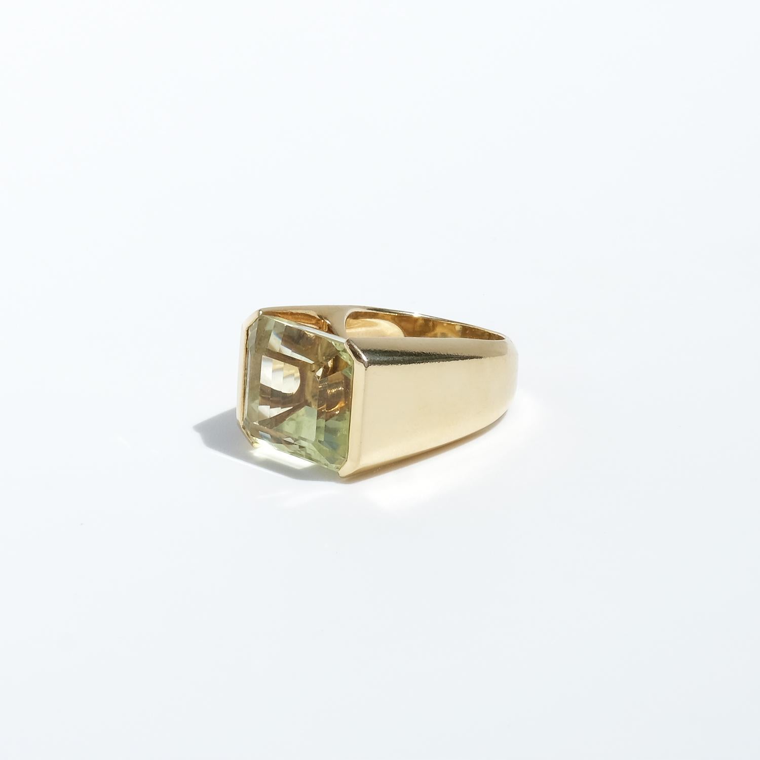 This 18-karat gold cocktail ring features a stunning emerald cut heliodor gemstone with a delicate greenish-yellow hue (approx. 26 ct). The stone is beautifully faceted on all sides, including the underside, which is gently curved, enhancing its