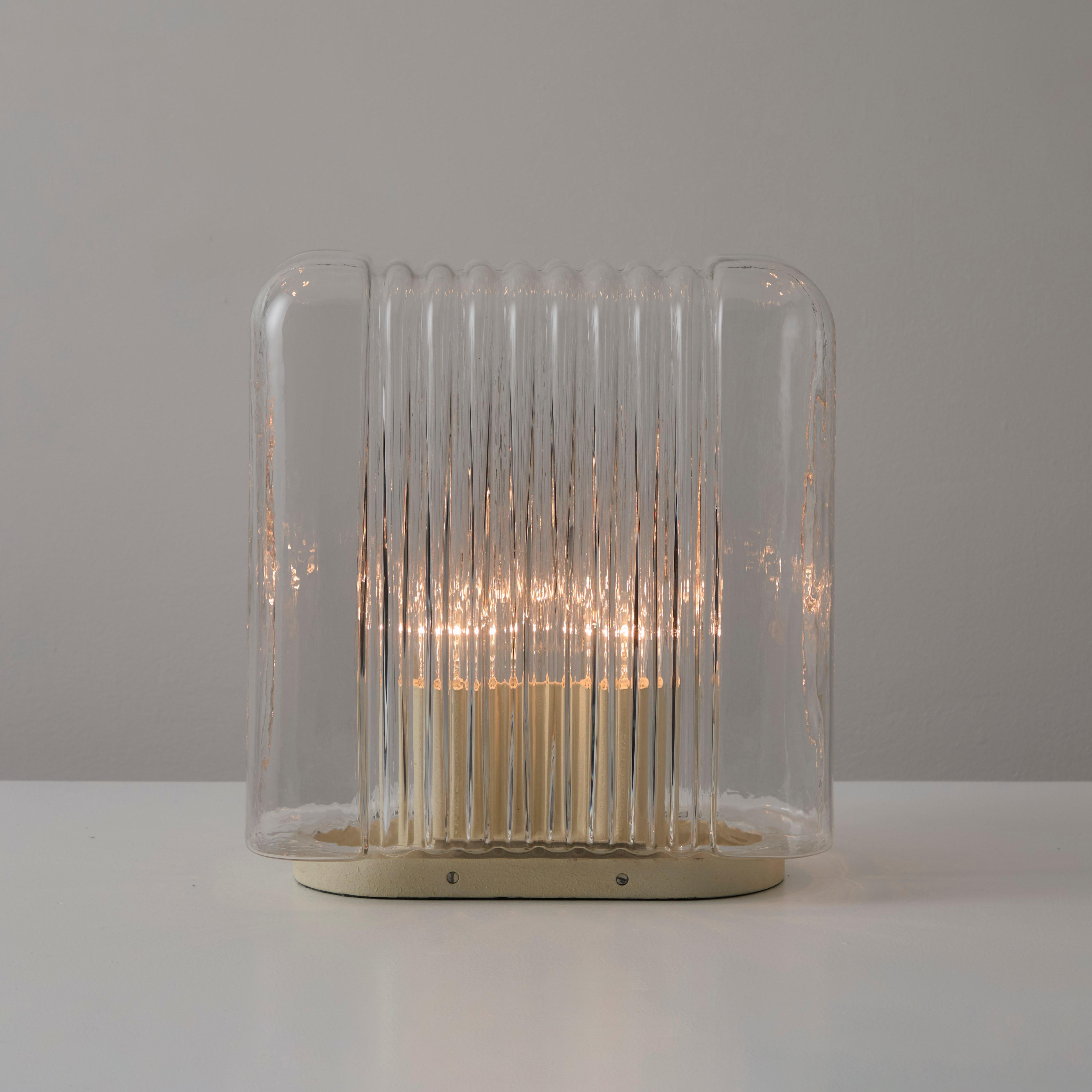 'Lari' Table Lamp by Angelo Mangiarotti for Artemide. Designed and manufactured in Italy, in 1969. Ribbed clear glass diffuser encloses over a double enameled socket housing. Two E27 socket-types make up the lamping on this iconic table lamp. Toggle
