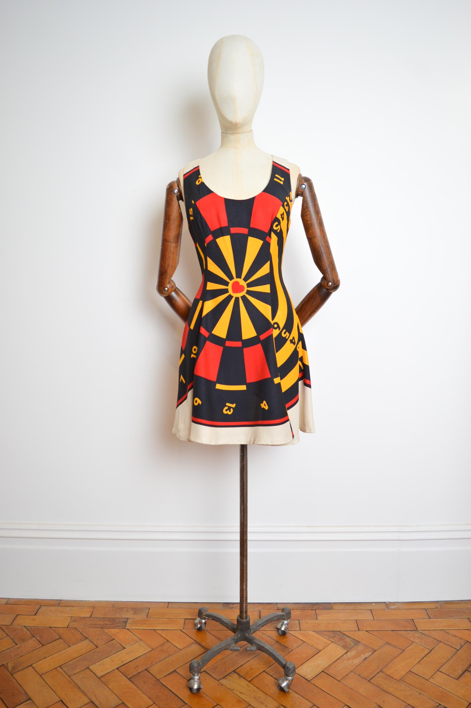 Moschino Cheap and Chic, stampa a freccette della roulette anni '90, mini abito a turni di Vega 
Un mini abito con stampa roulette di Moschino 'Cheap and Chic' nei toni del bianco sporco, del giallo e del rosso.
MADE IN ITALY
Chiusura posteriore con