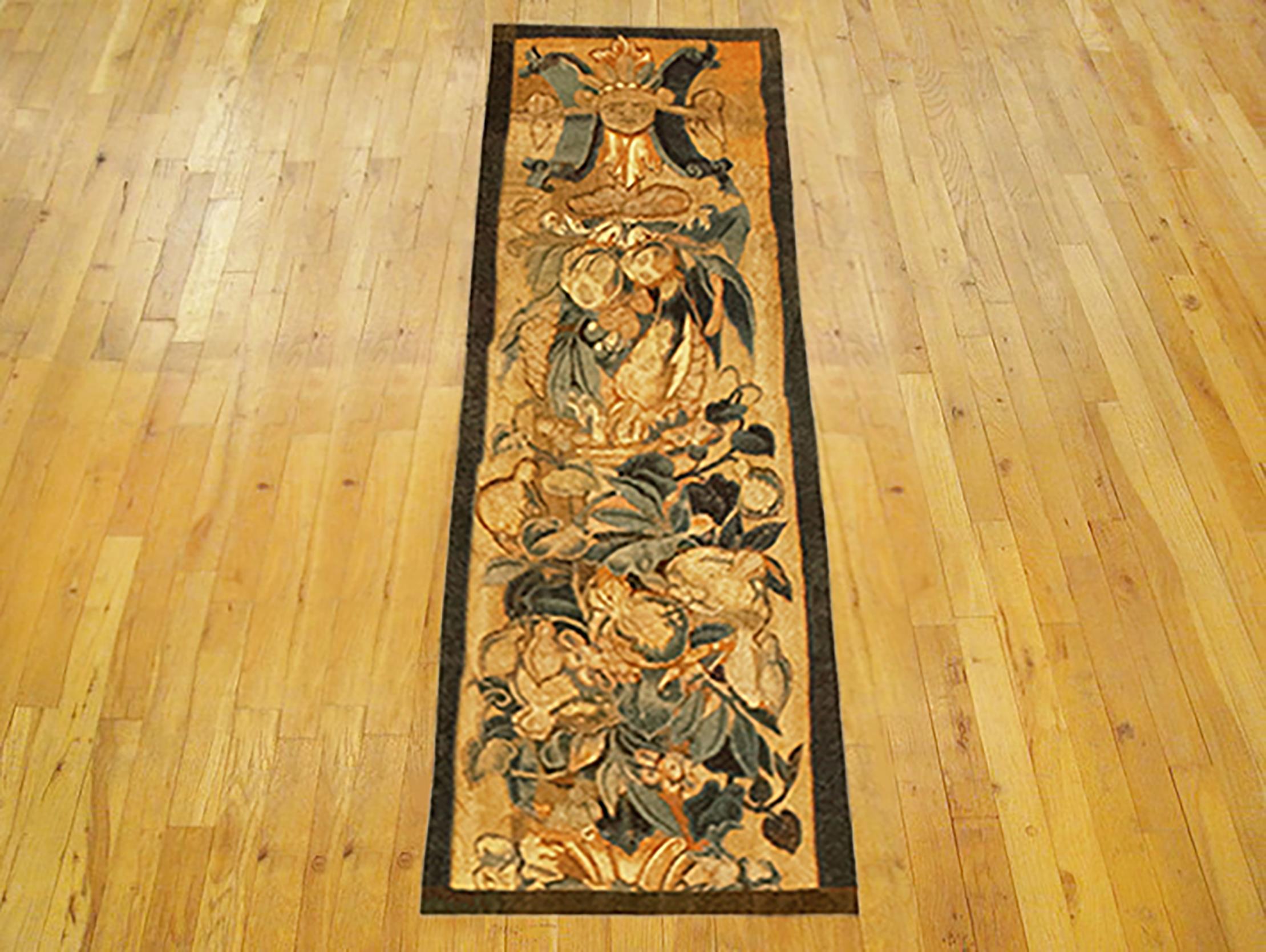 A 16th Century Brussels historical tapestry panel. This vertically oriented decorative tapestry panel depicts a scrolling foliate design, with a grotesque and a coat of arms at top, and with ribbon ties and acanthus leaves below. The central area is