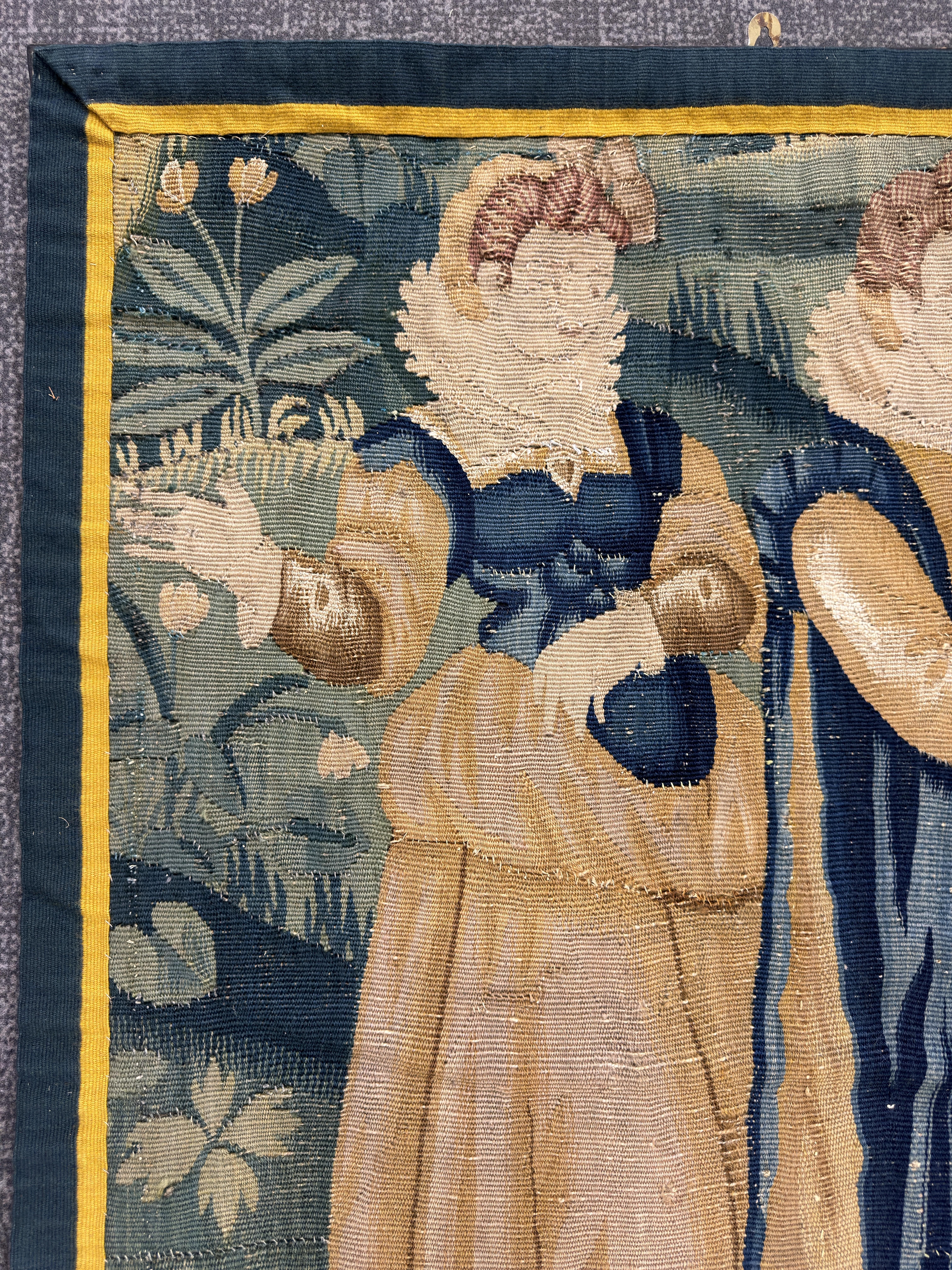 Late 16th/Early 17th Century Tapestry Fragment Wall Hanging depicting two elegantly dressed female courtiers in a garden landscape, edged in a later ochre and blue border band.