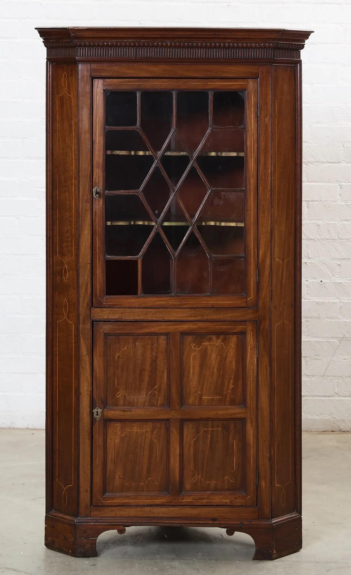 Late 18th Century American Federal Inlaid Mahogany Corner Cabinet with an overhanging dentil molded cornice above the upper section with a diamond pattern individually glazed divided lite door opening to a compartment with two shelves. The lower