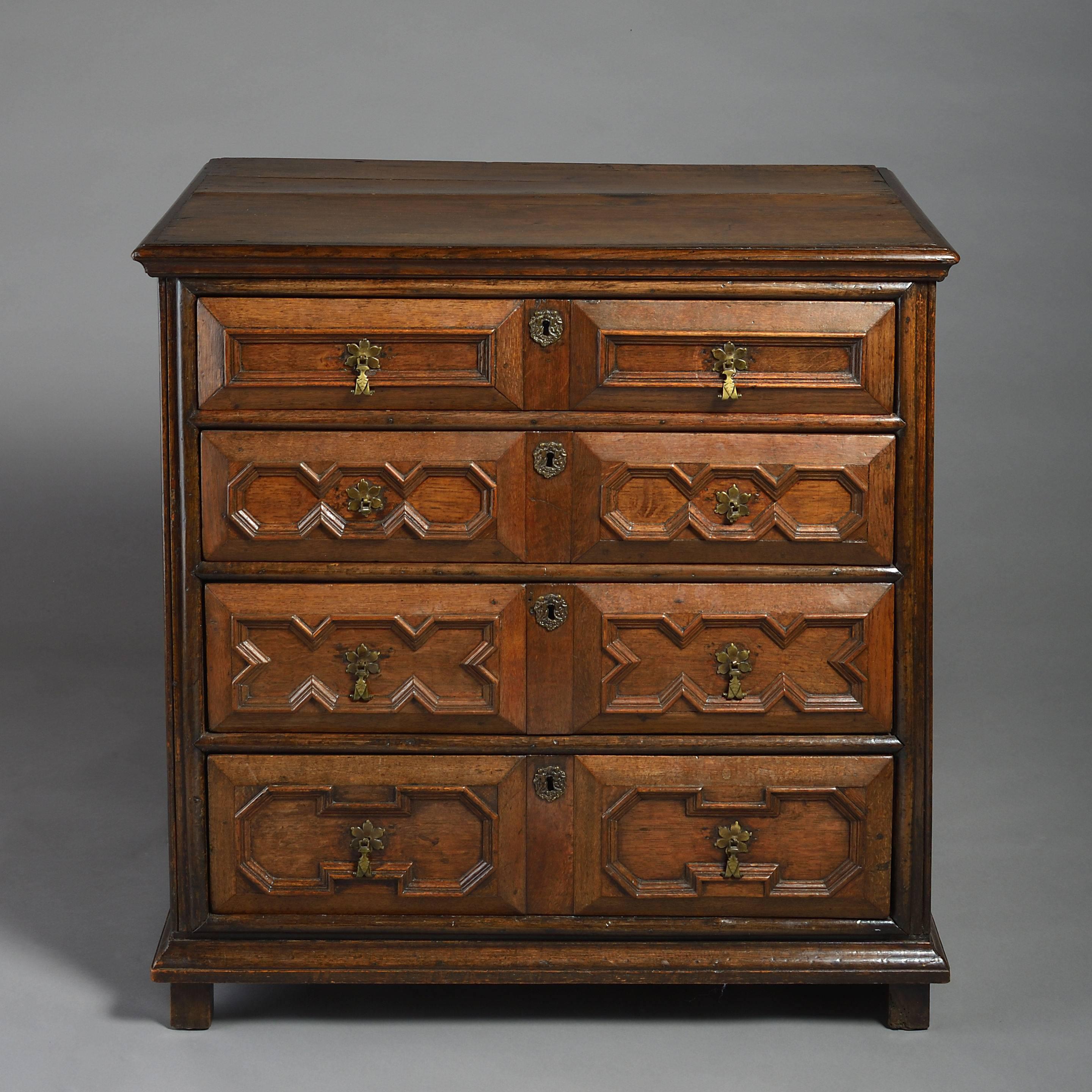 A late 17th century Charles II period oak chest of drawers, the overhanging top above four drawers, each with geometric mouldings, drop handles and lock escutcheons.